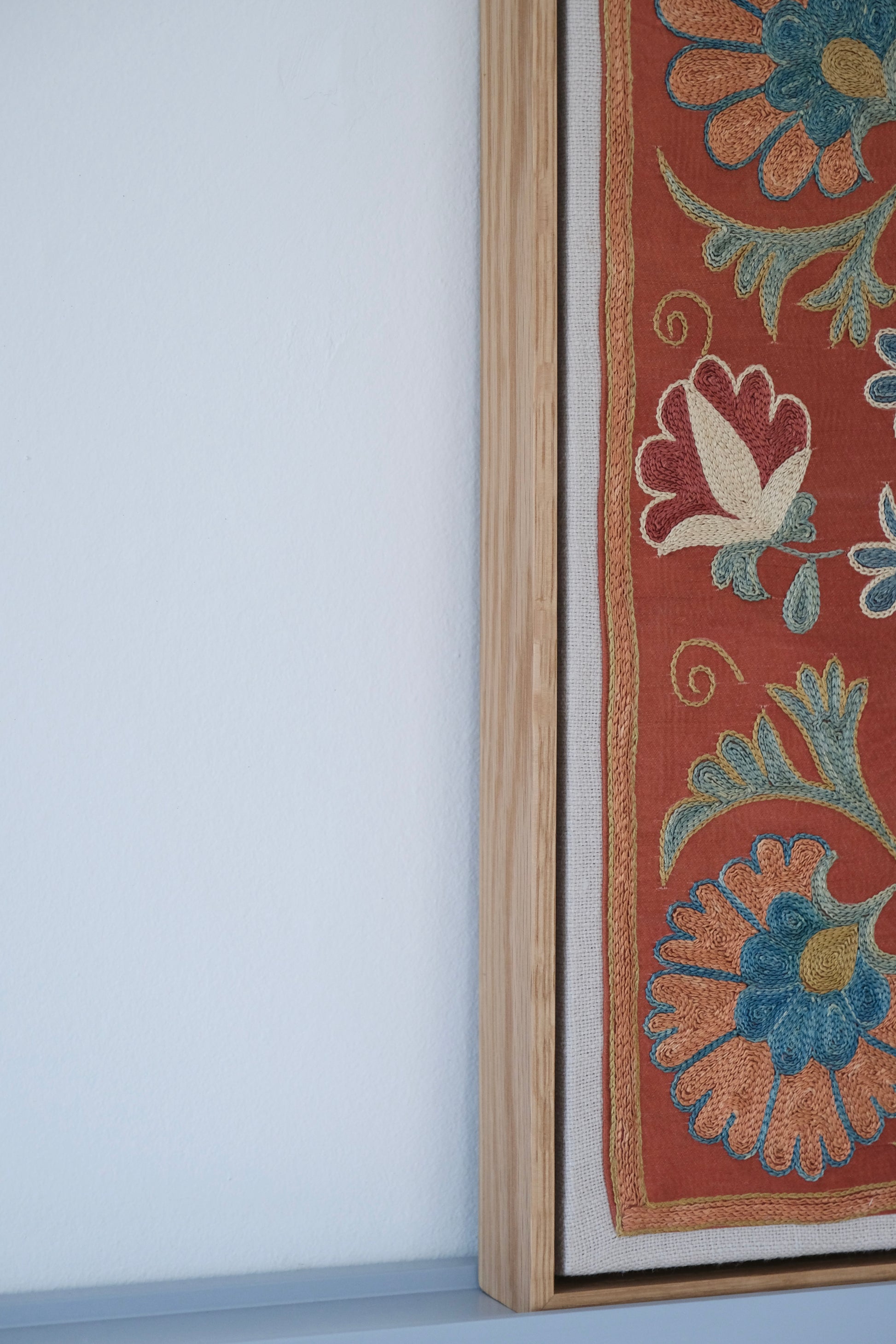 Framed suzani, embroidered textile art, wooden frame, dark orange with blue and green floral motifs, side view
