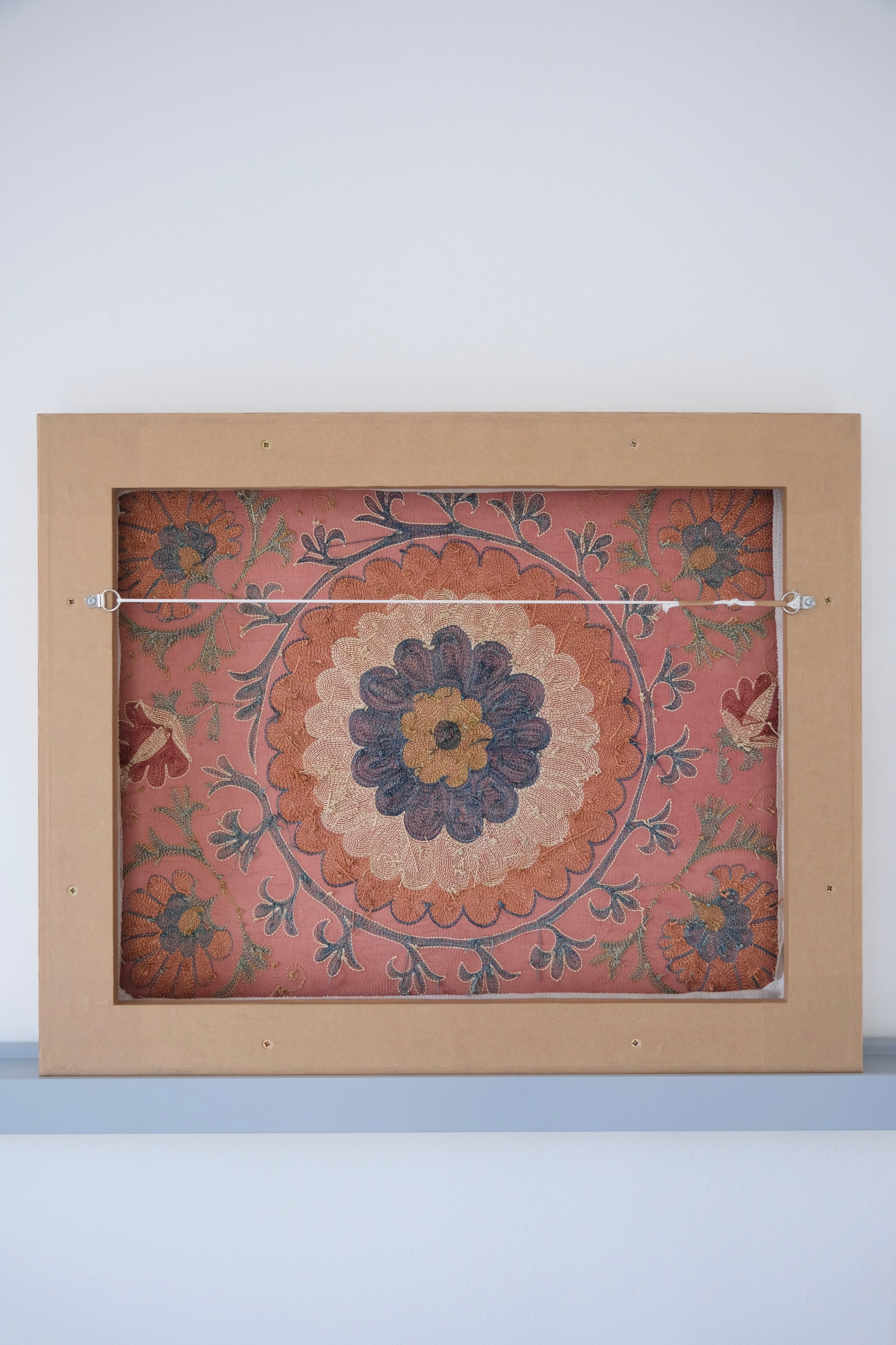 Framed suzani, embroidered textile art, wooden frame, dark orange with blue and green floral motifs, backside