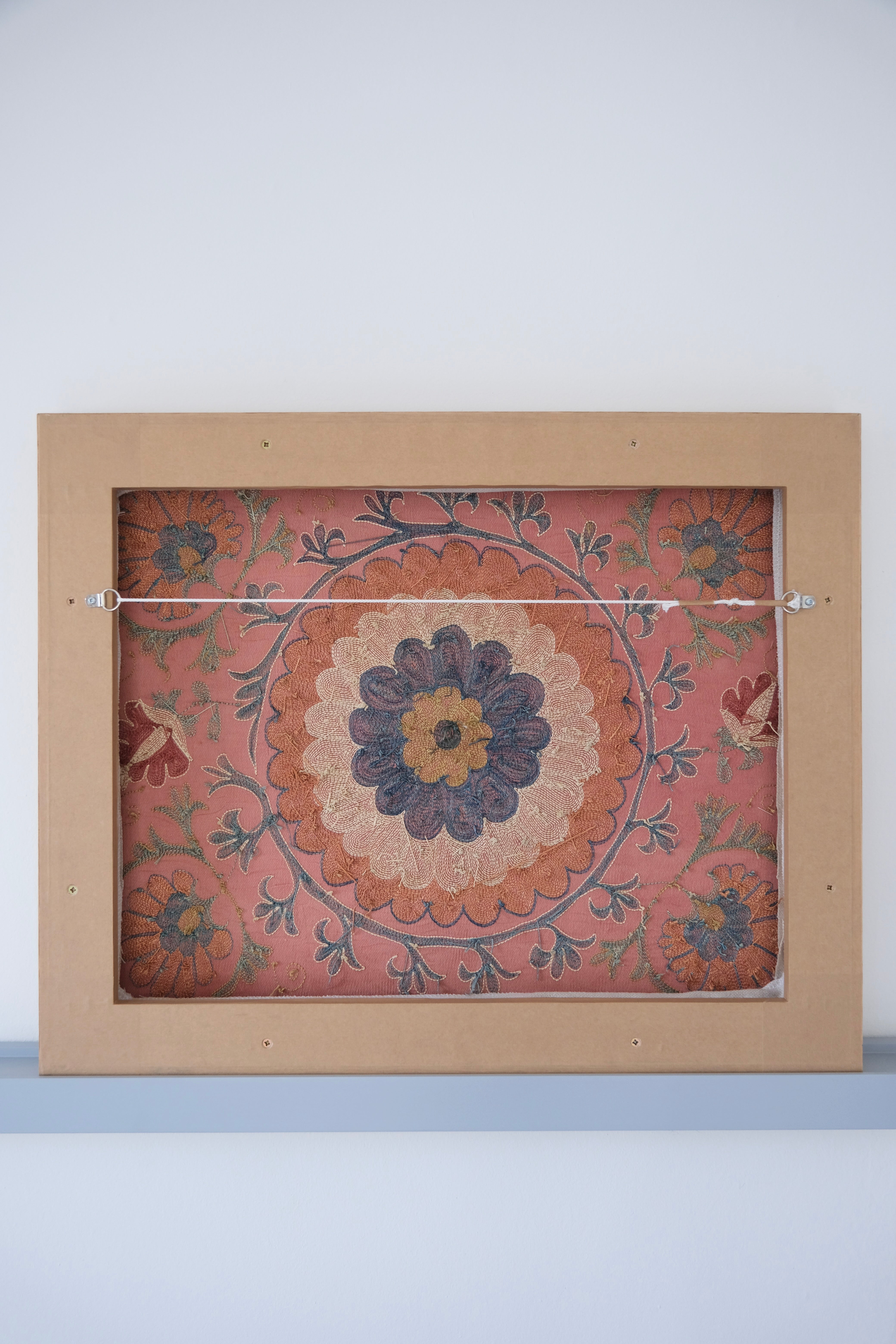 Framed suzani, embroidered textile art, wooden frame, dark orange with blue and green floral motifs, backside