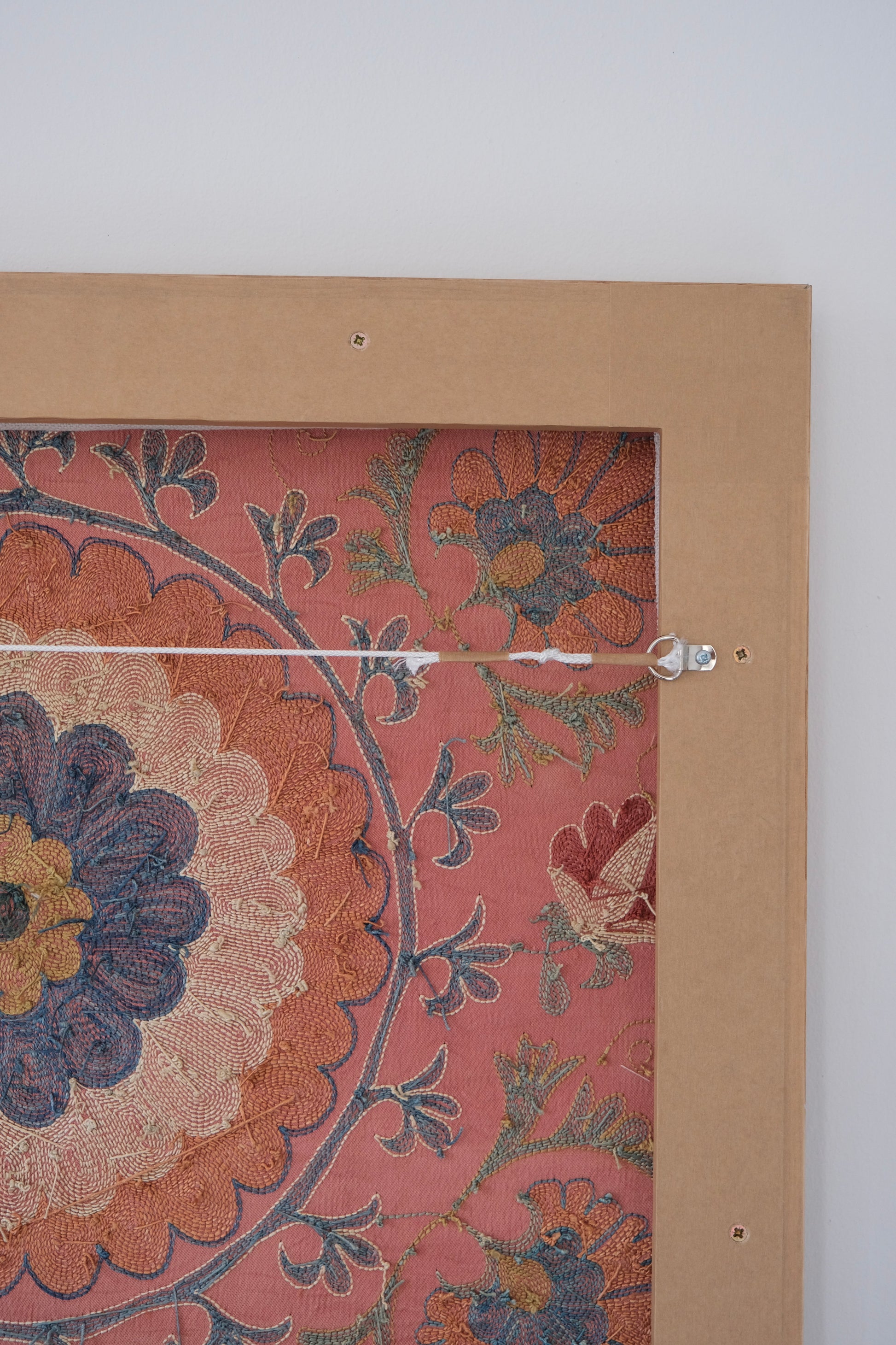 Framed suzani, embroidered textile art, wooden frame, dark orange with blue and green floral motifs, backside