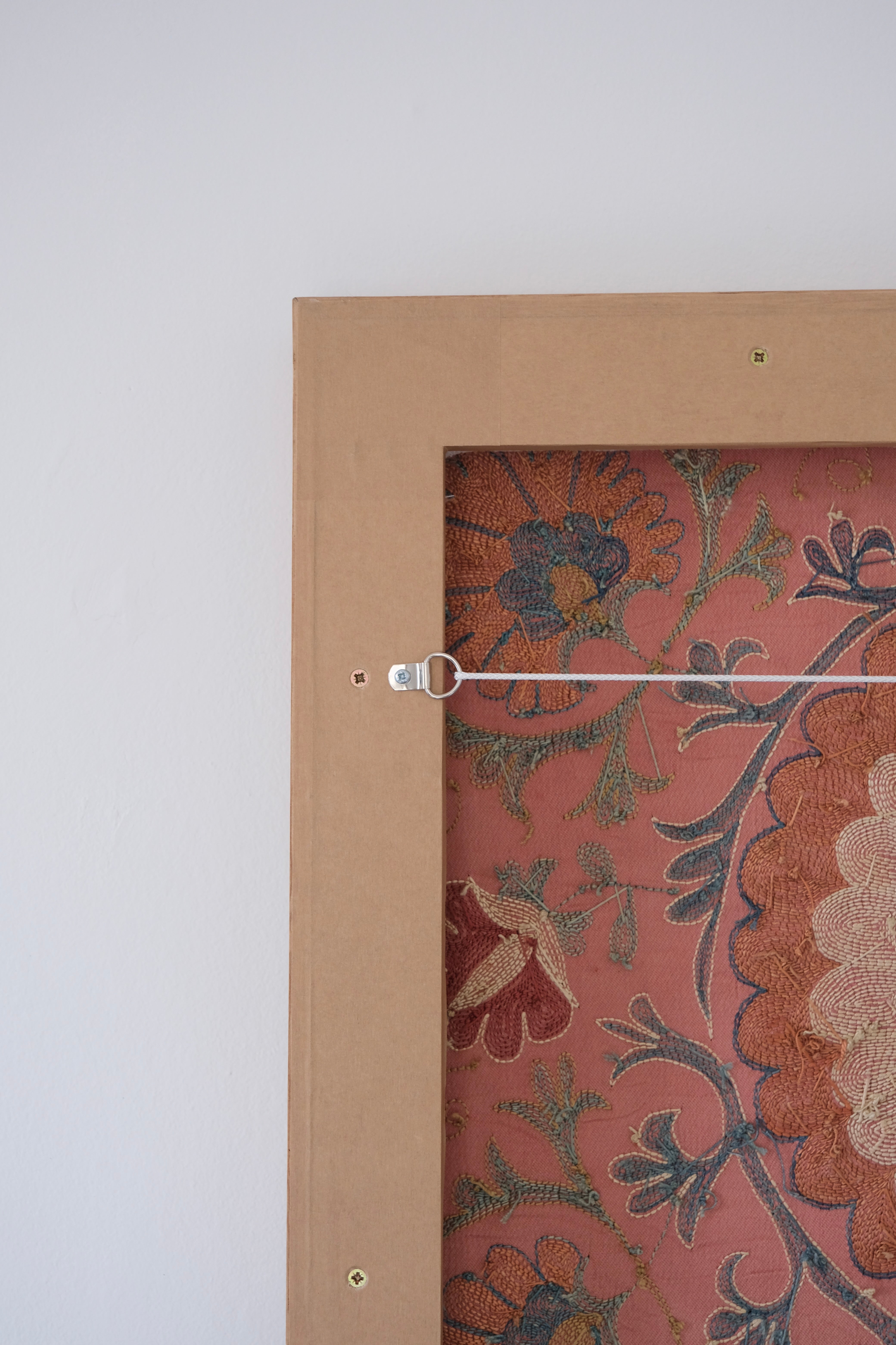 Framed suzani, embroidered textile art, wooden frame, dark orange with blue and green floral motifs, backside
