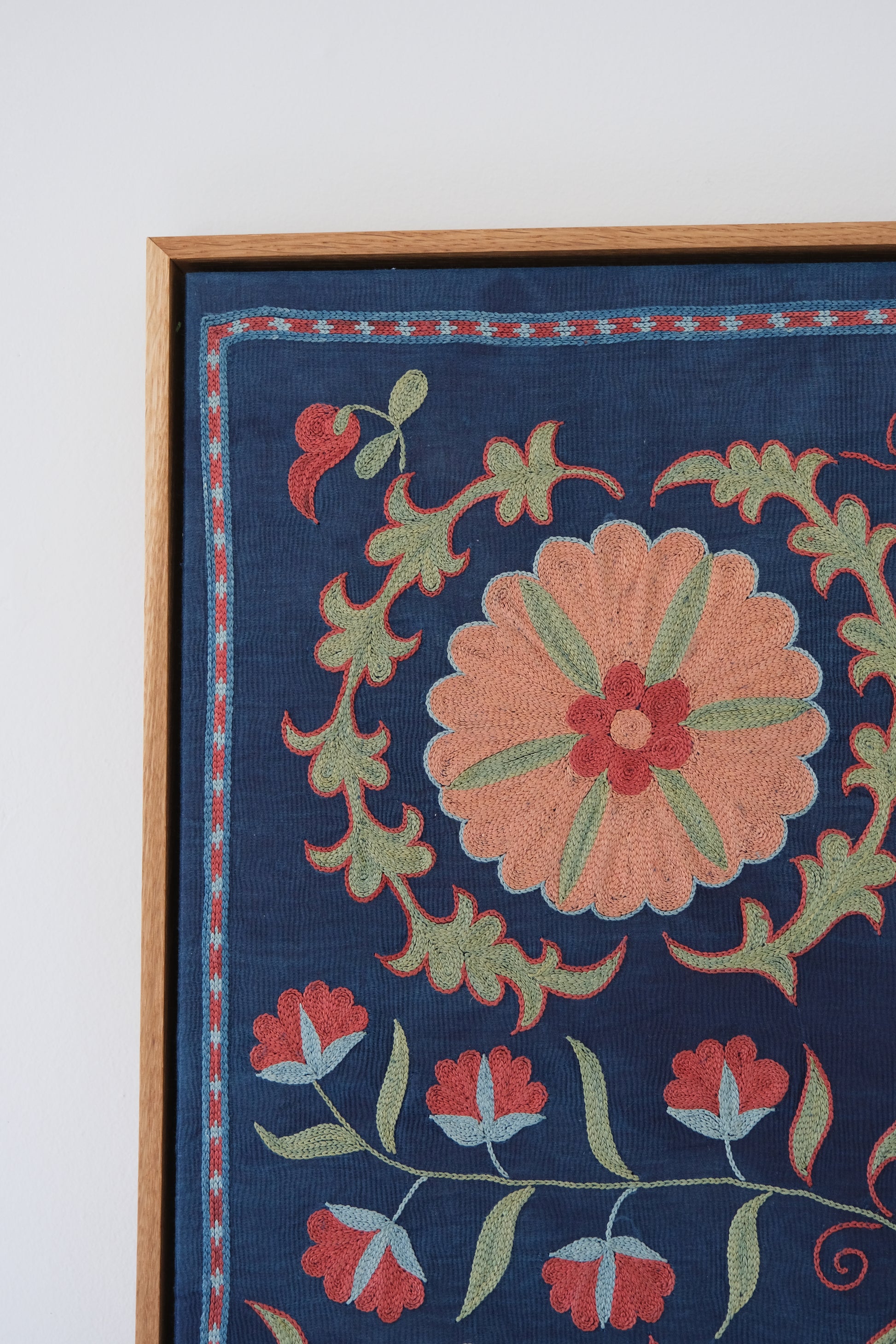 Framed suzani, embroidered textile art, wooden frame, navy blue with floral motifs, close-up
