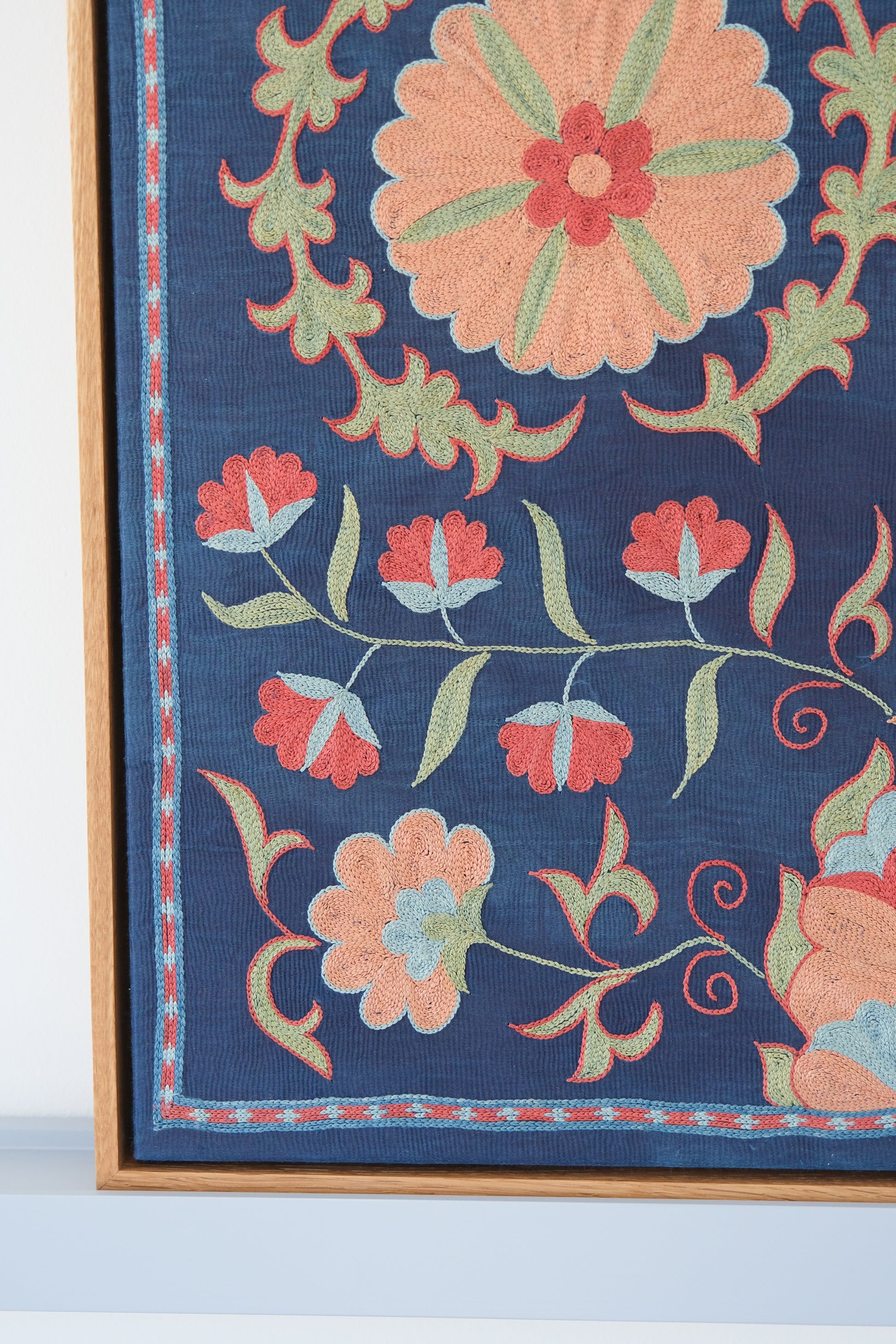 Framed suzani, embroidered textile art, wooden frame, navy blue with floral motifs, close-up