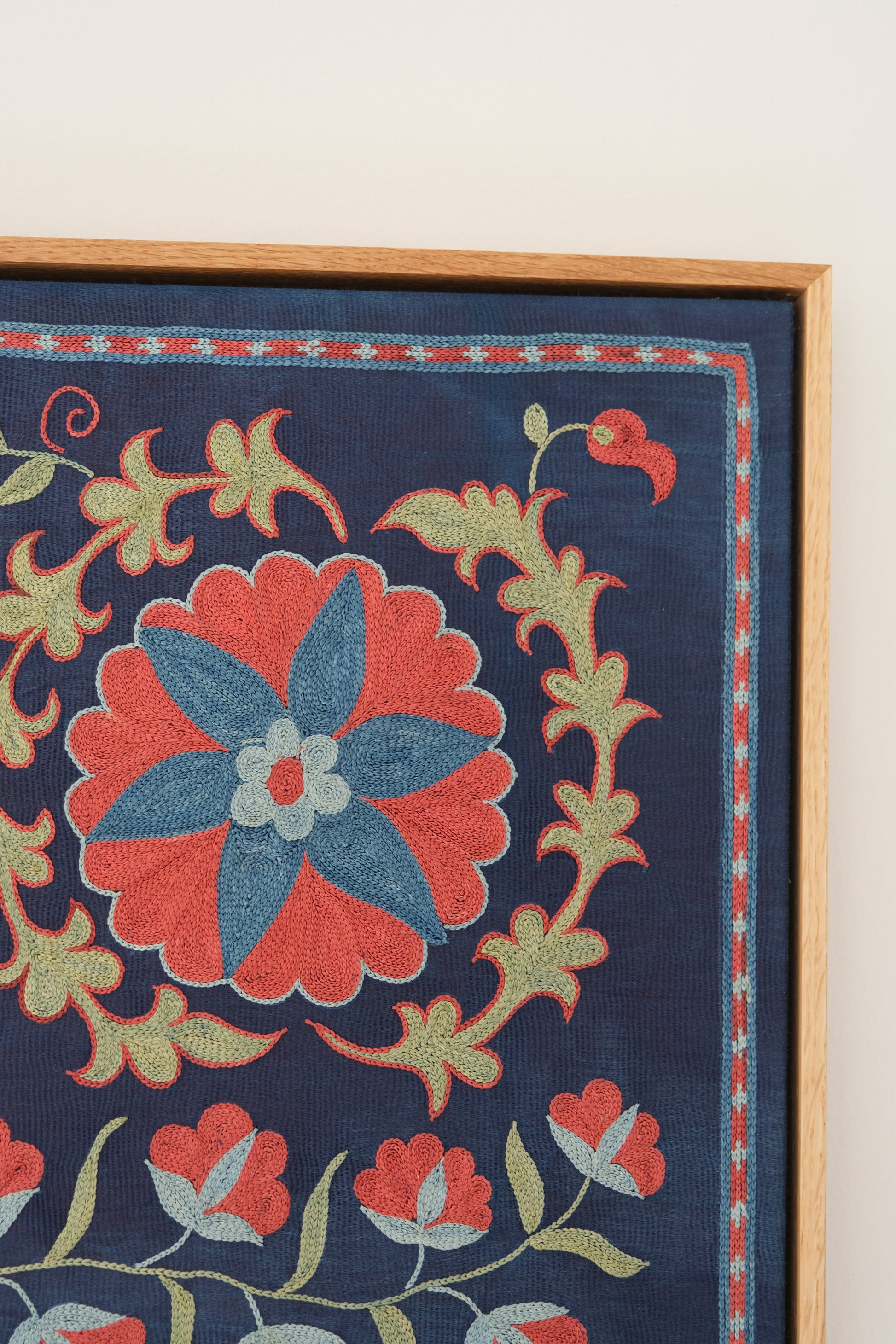Framed suzani, embroidered textile art, wooden frame, navy blue with floral motifs, close-up