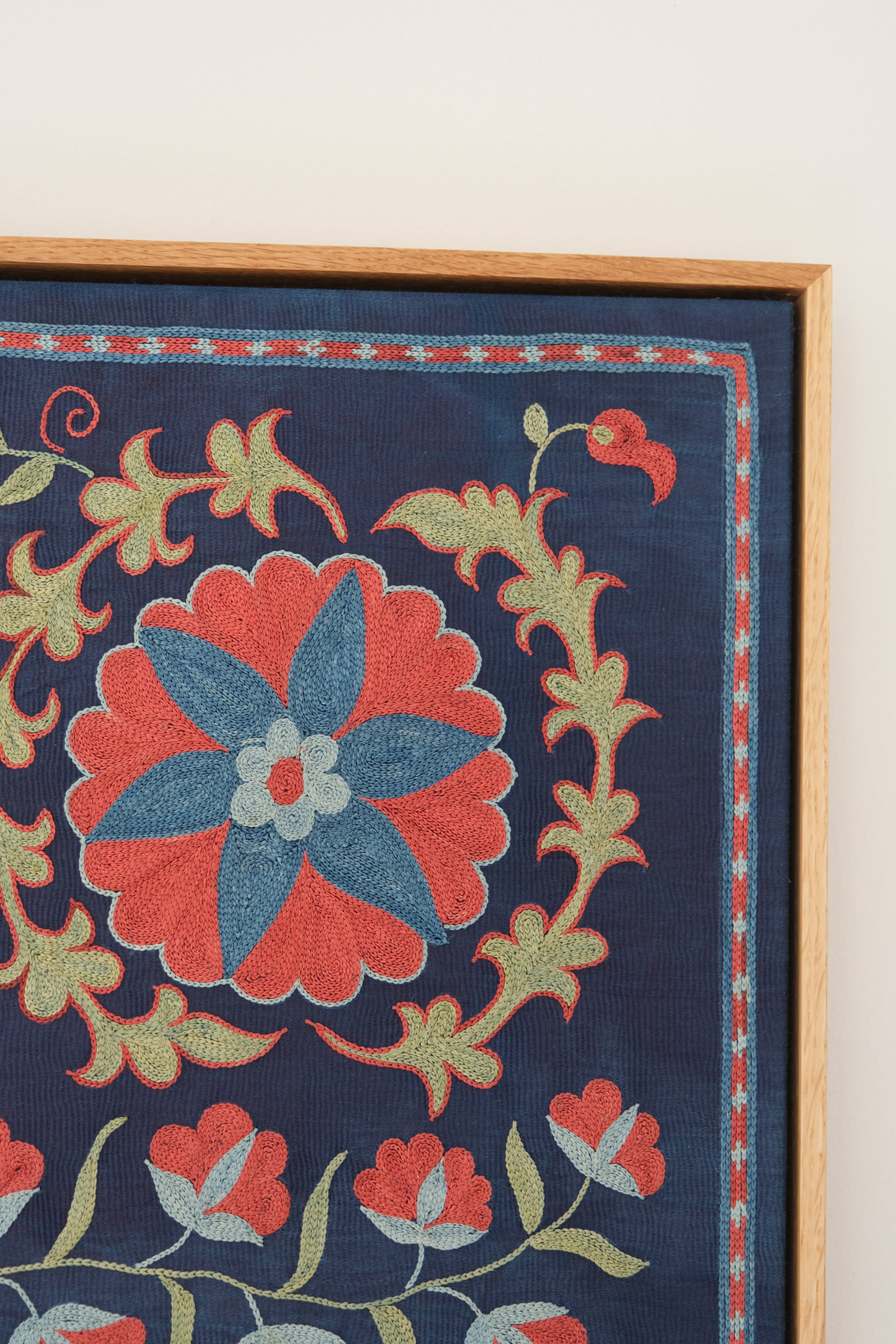 Framed suzani, embroidered textile art, wooden frame, navy blue with floral motifs, close-up