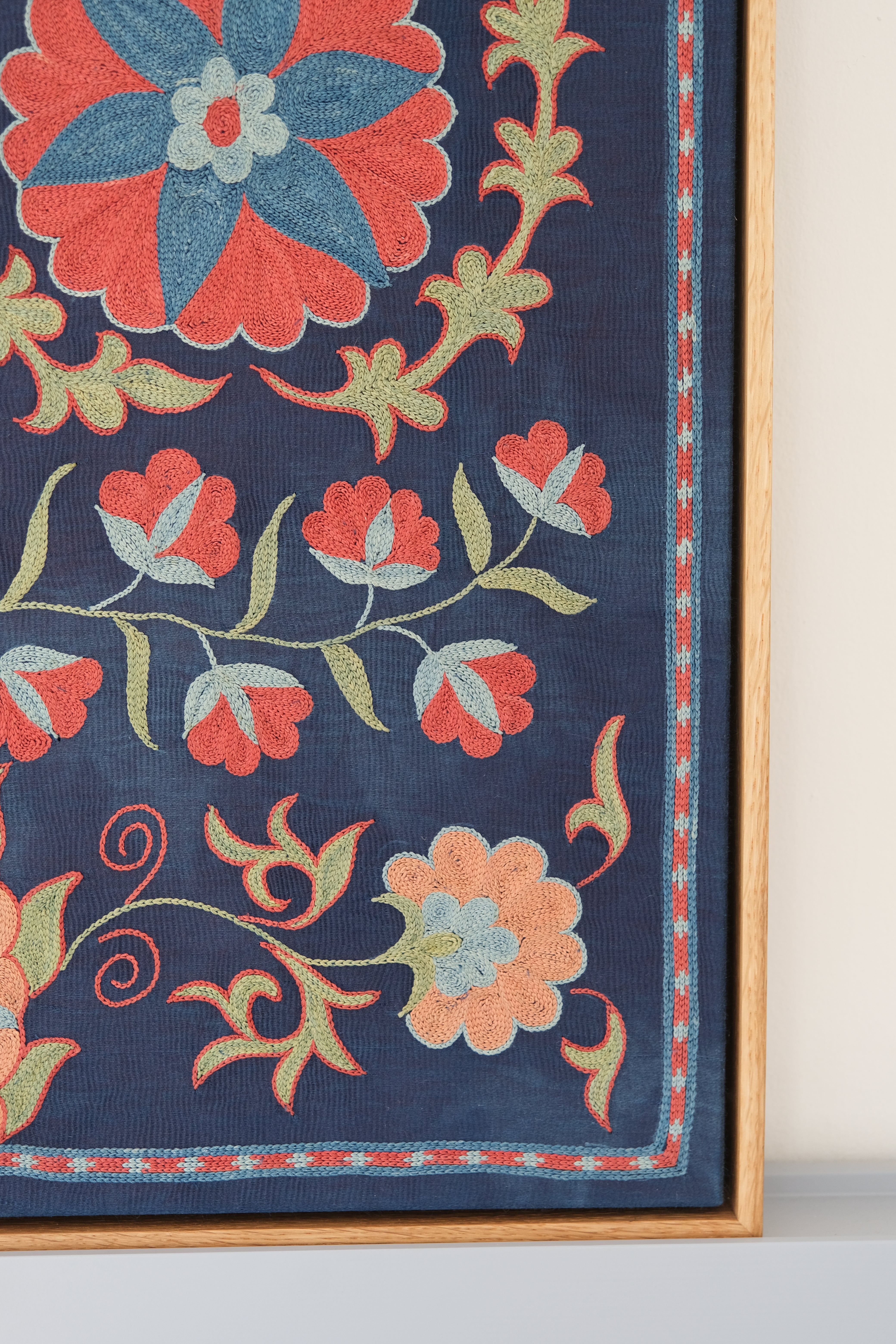 Framed suzani, embroidered textile art, wooden frame, navy blue with floral motifs, close-up