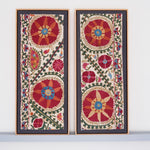 Two framed antique suzanis, embroidered textile artworks with floral patterns on a white background