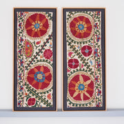 Two framed antique suzanis, embroidered textile artworks with floral patterns on a white background