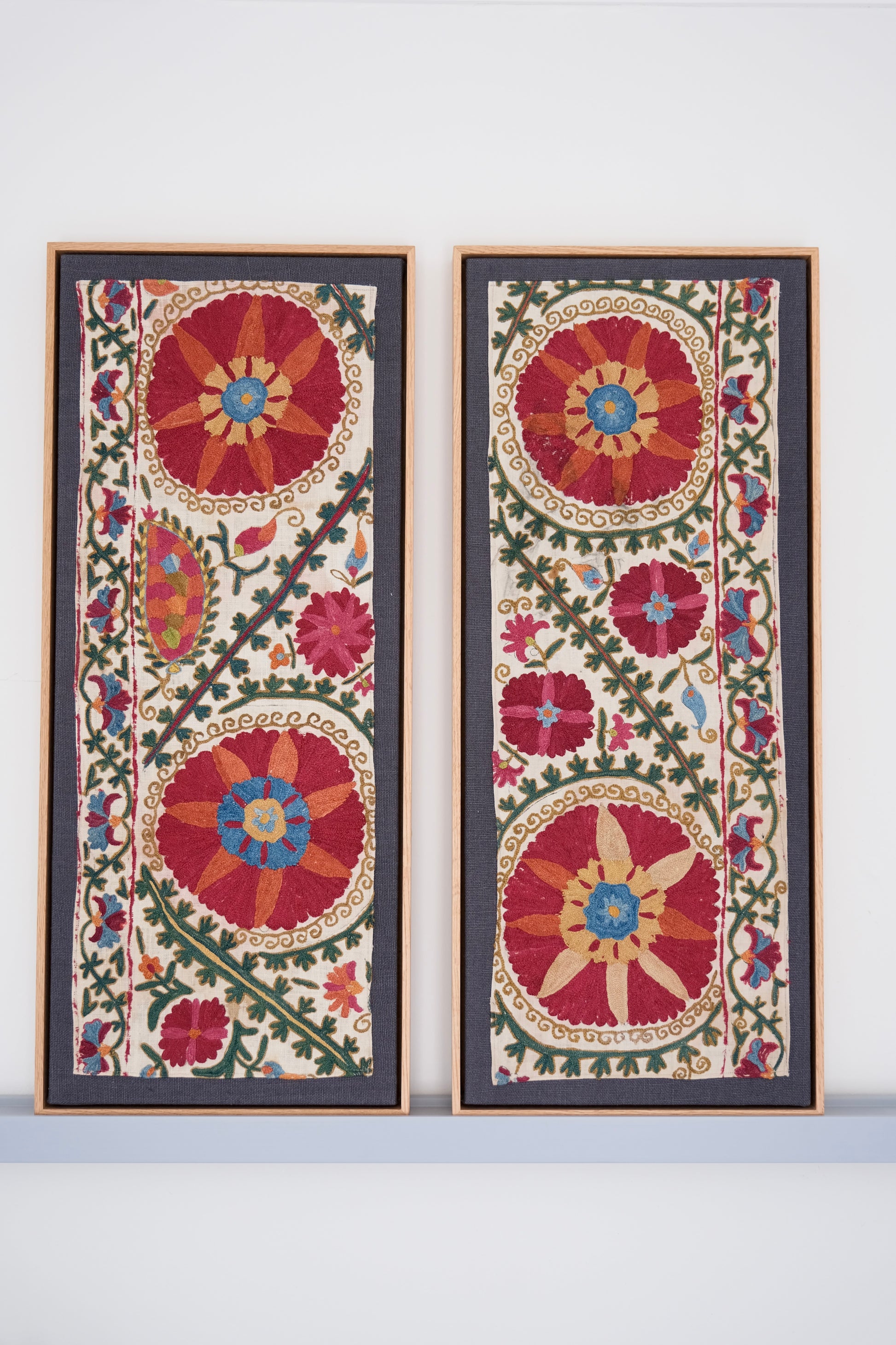 Two framed antique suzanis, embroidered textile artworks with floral patterns on a white background