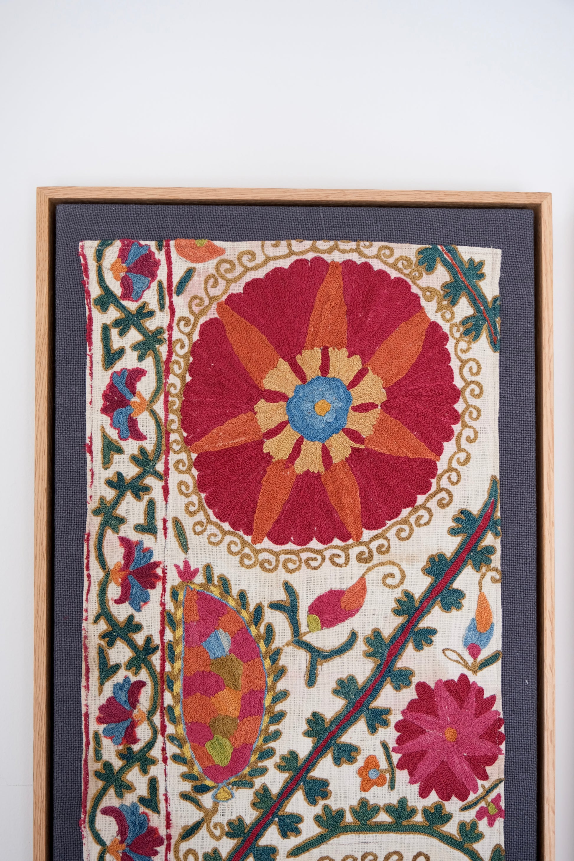 Framed embroidered textile with floral patterns on a white background