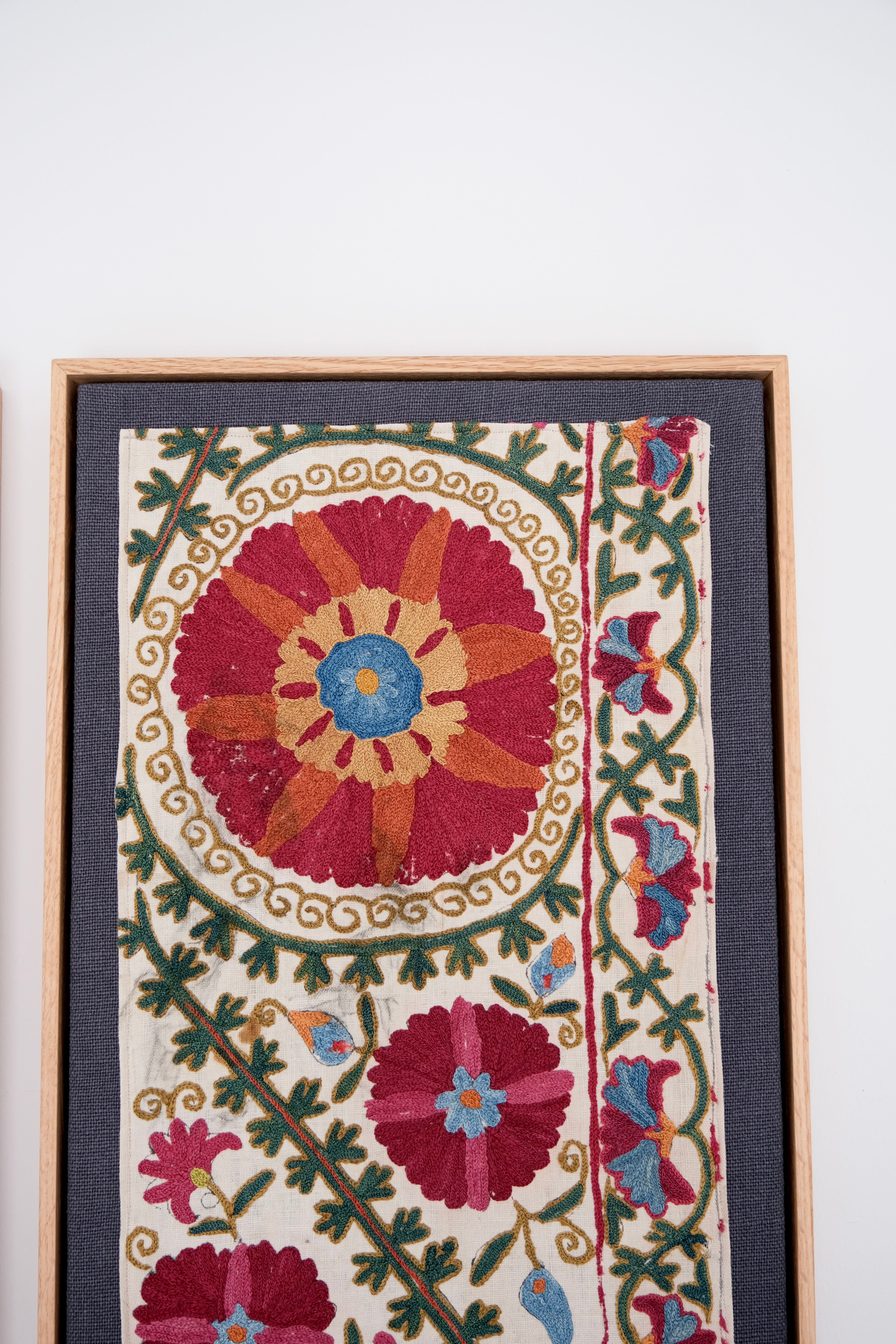 Framed embroidered textile with floral patterns on a white background