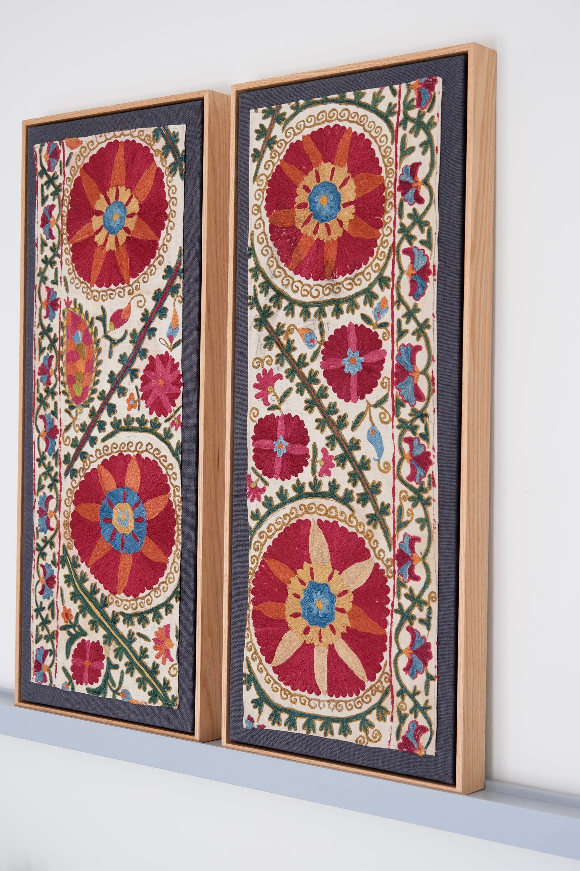 Two framed antique suzanis, embroidered textile artworks with floral patterns on a white background