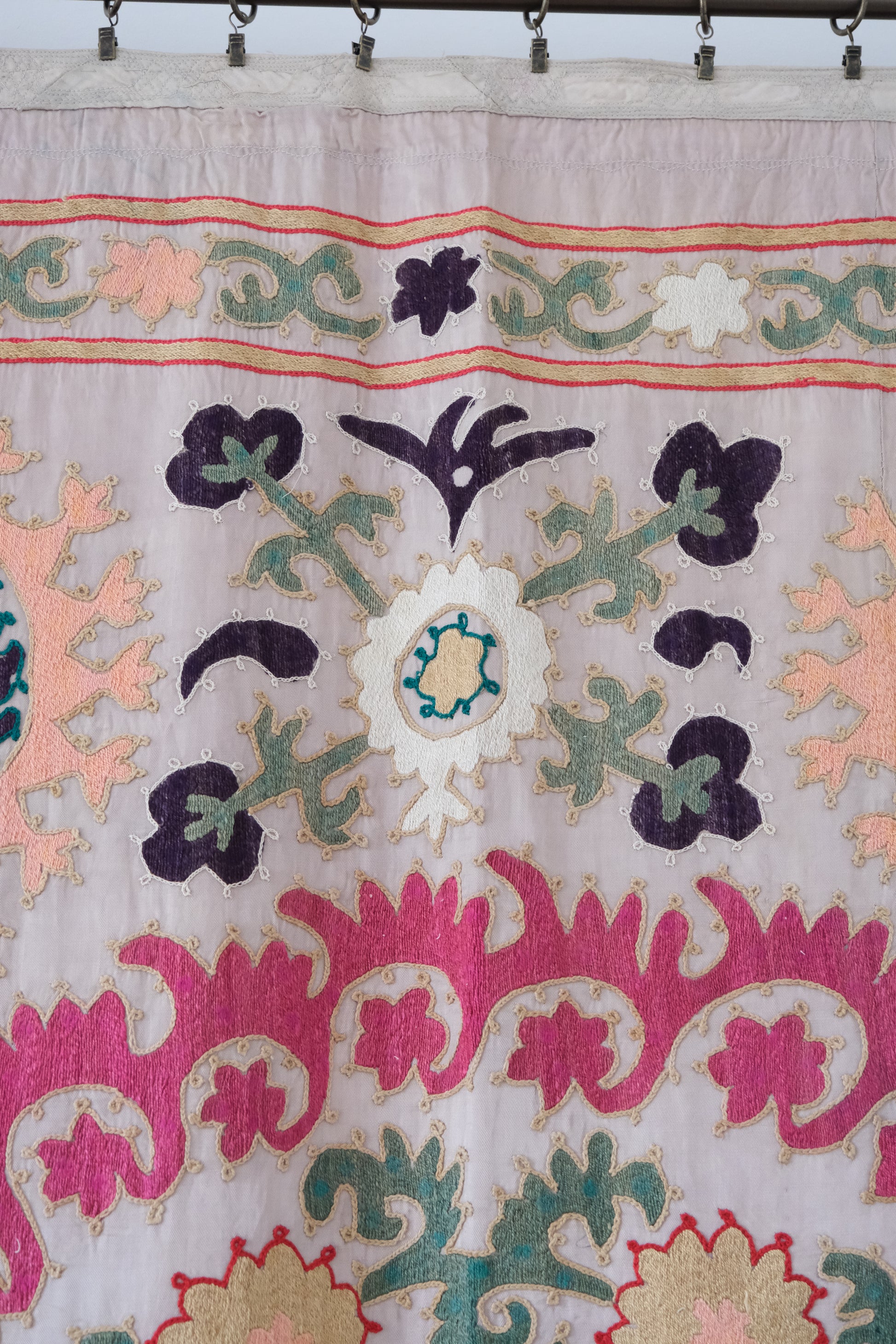 Vintage suzani, decorative embroidered tapestry, pink with geometric and floral design, close-up