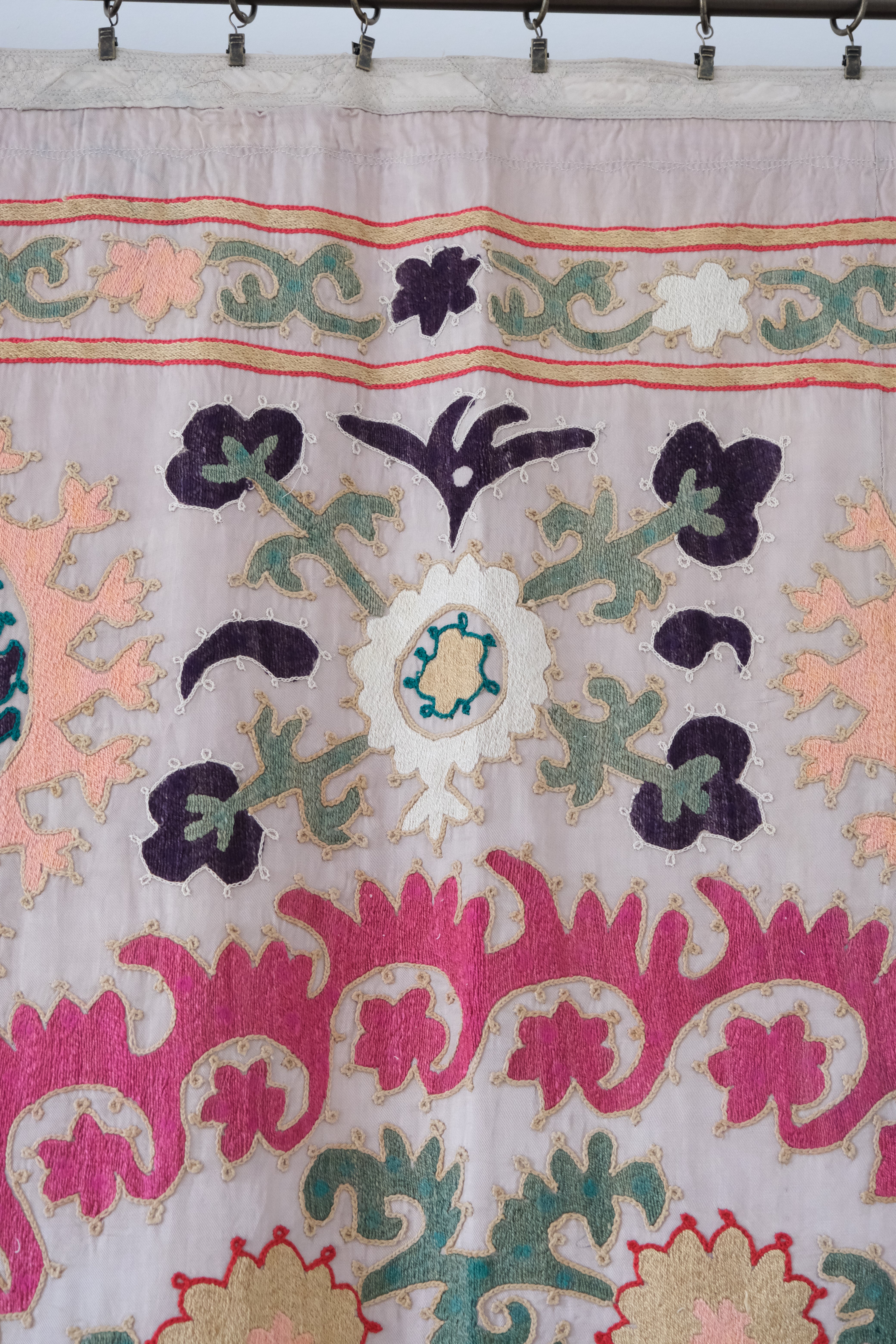 Vintage suzani, decorative embroidered tapestry, pink with geometric and floral design, close-up