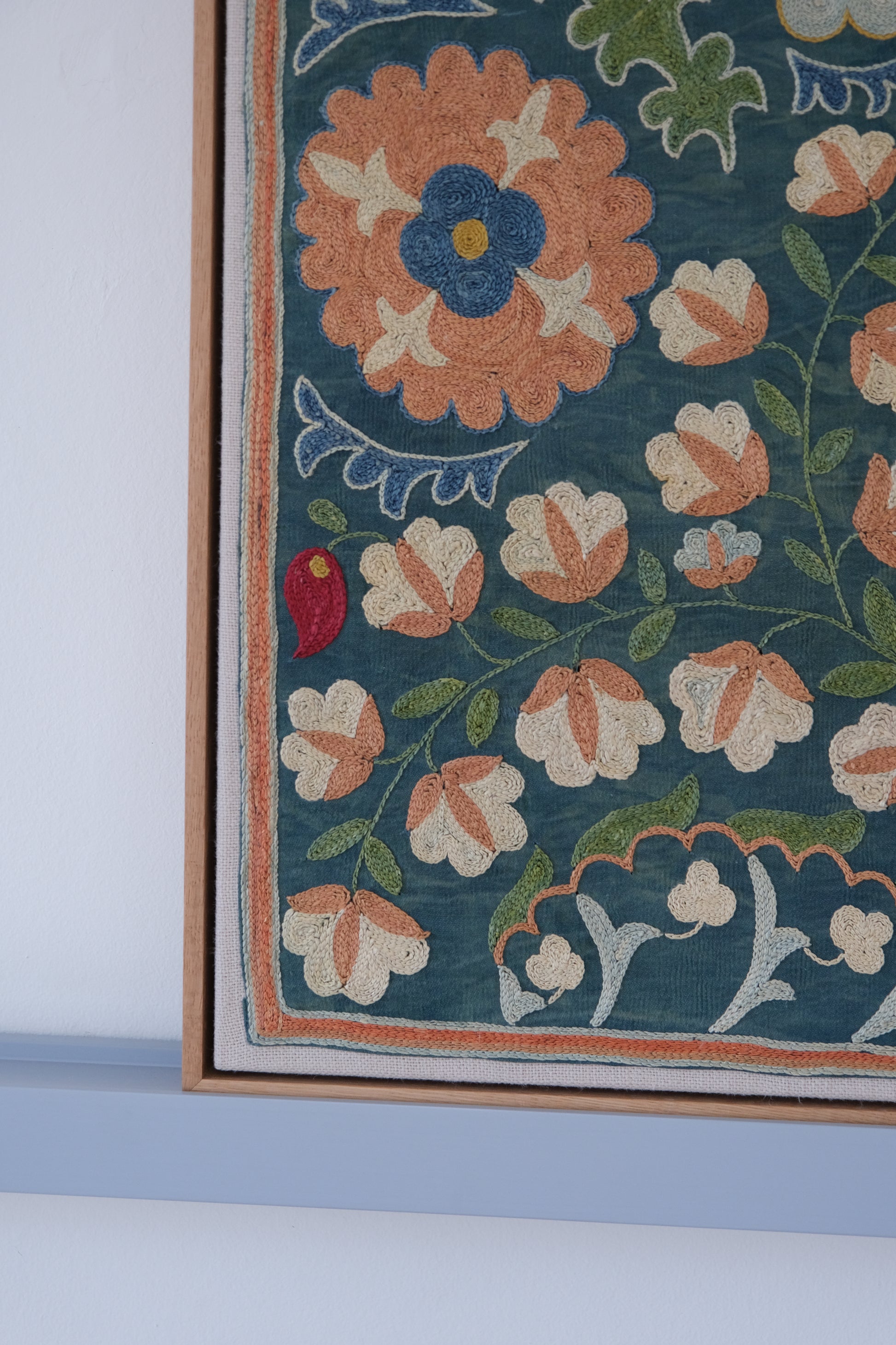 Framed suzani, embroidered textile art, wooden frame, green with orange and blue floral motifs, close-up