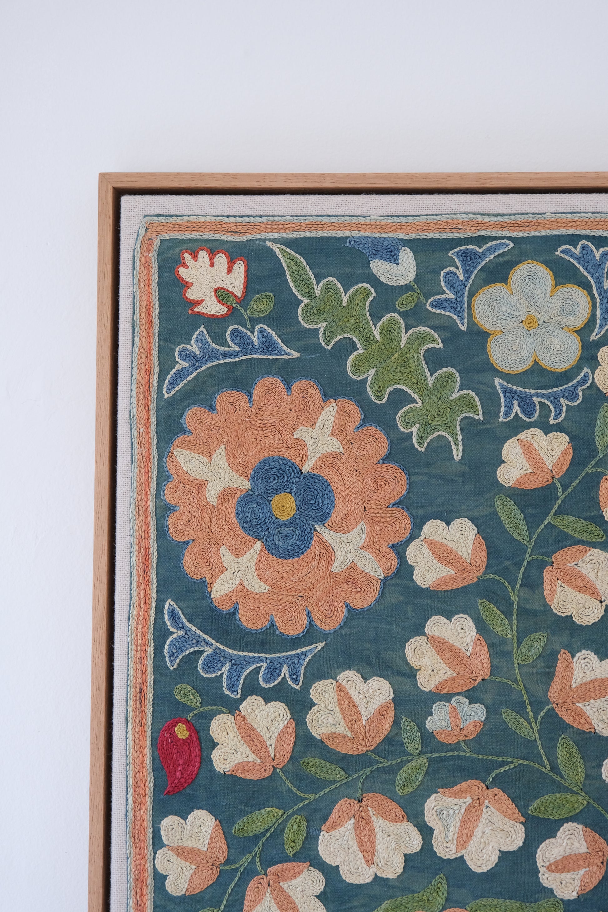 Framed suzani, embroidered textile art, wooden frame, green with orange and blue floral motifs, close-up