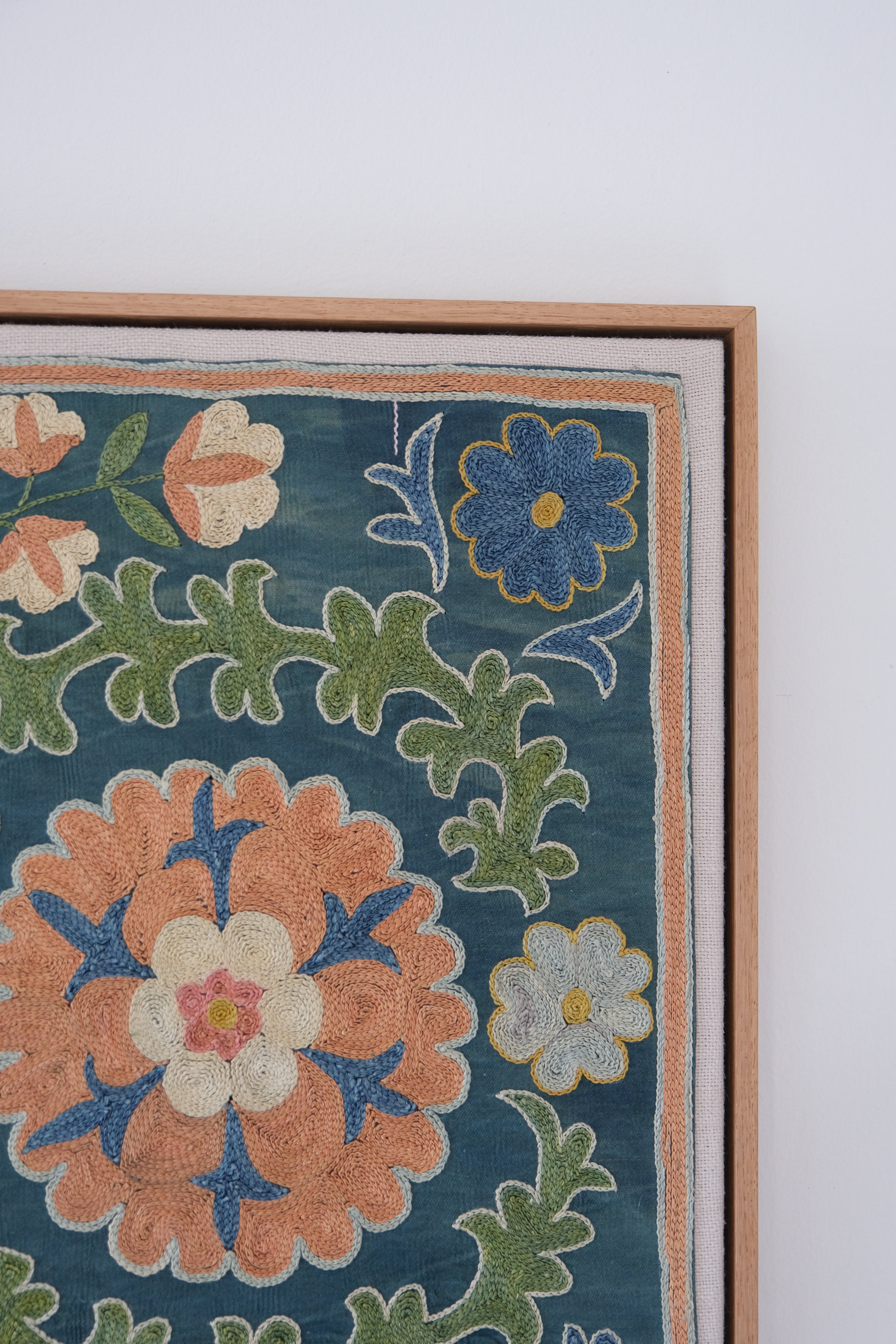 Framed suzani, embroidered textile art, wooden frame, green with orange and blue floral motifs, close-up