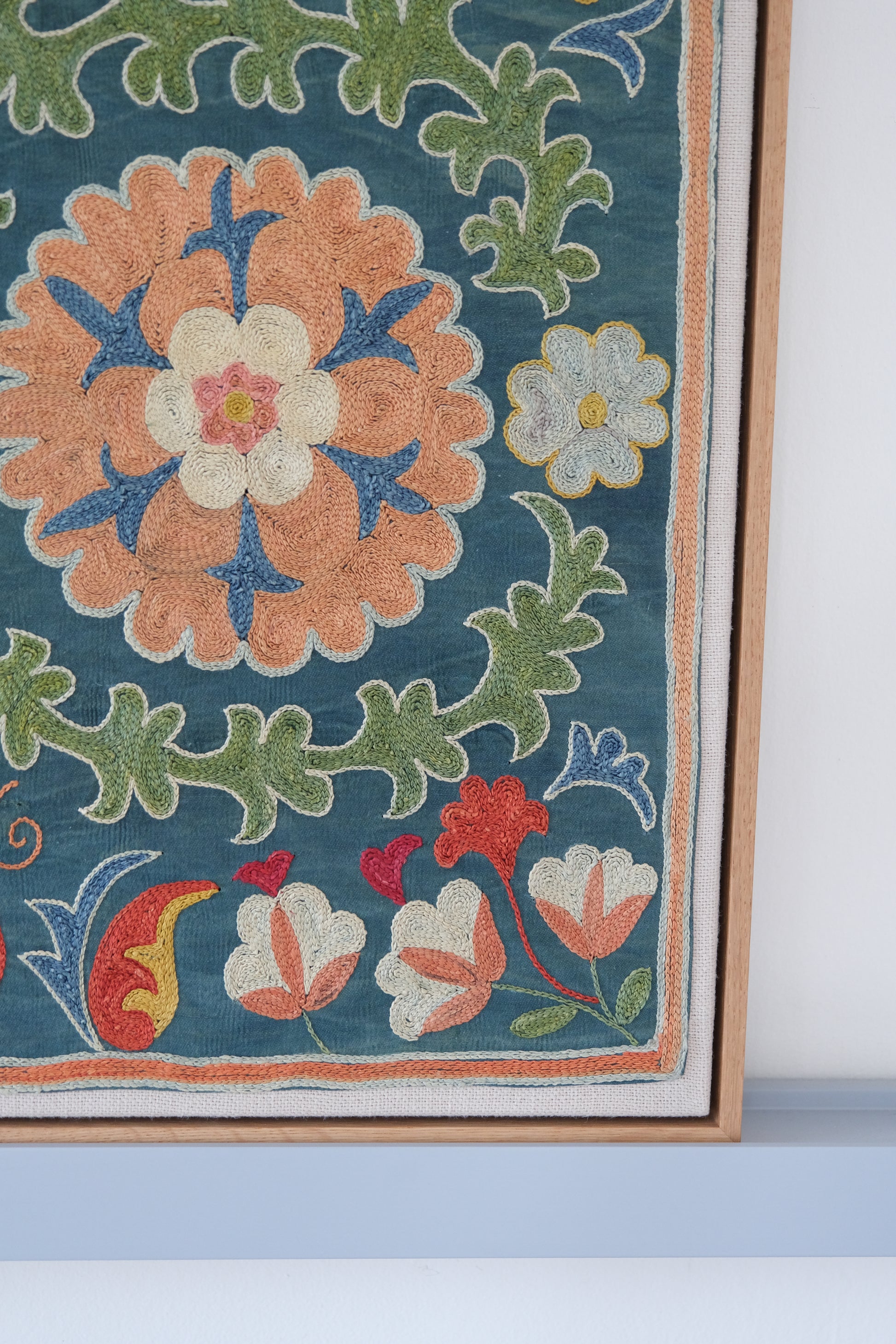 Framed suzani, embroidered textile art, wooden frame, green with orange and blue floral motifs, close-up