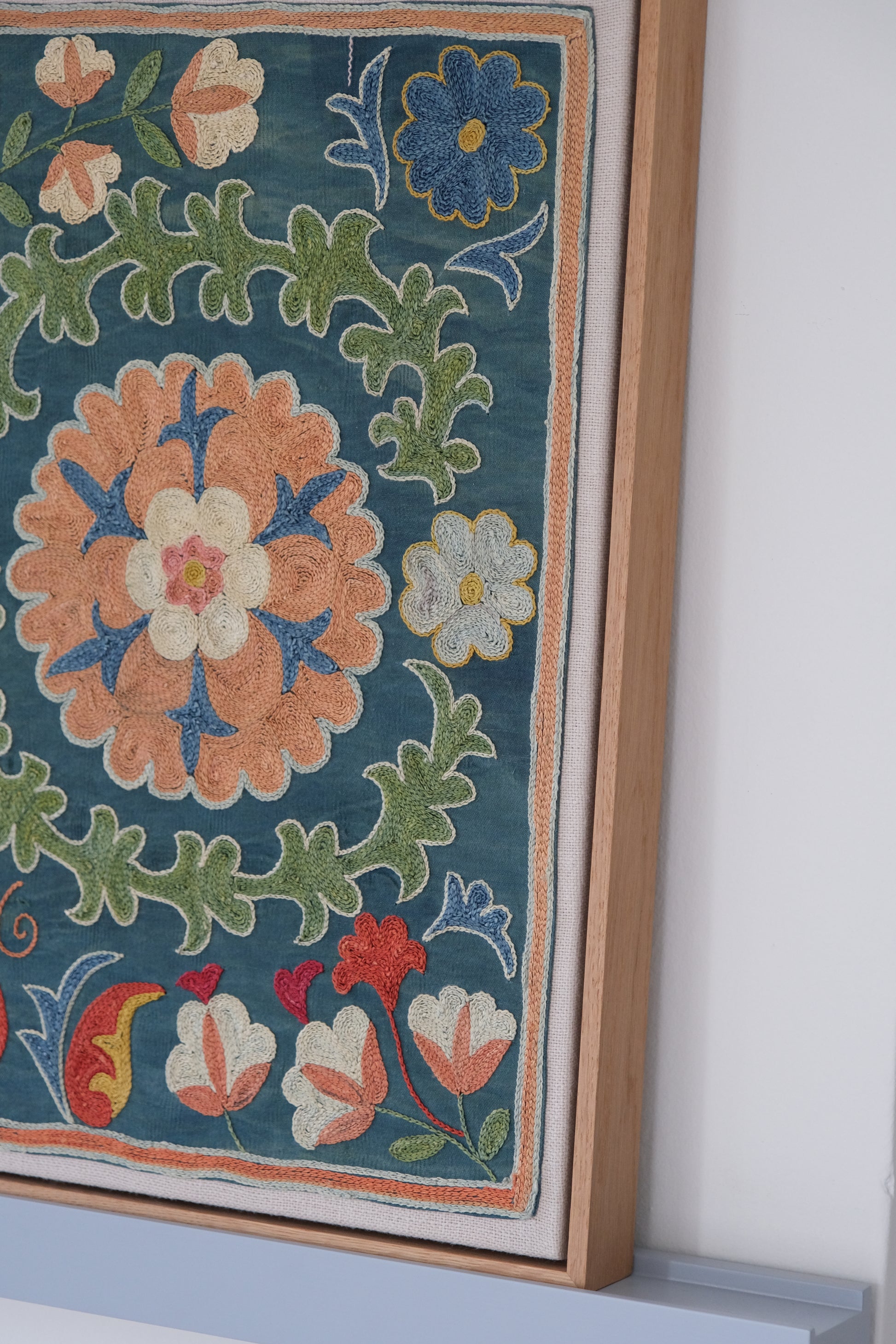 Framed suzani, embroidered textile art, wooden frame, green with orange and blue floral motifs, side view