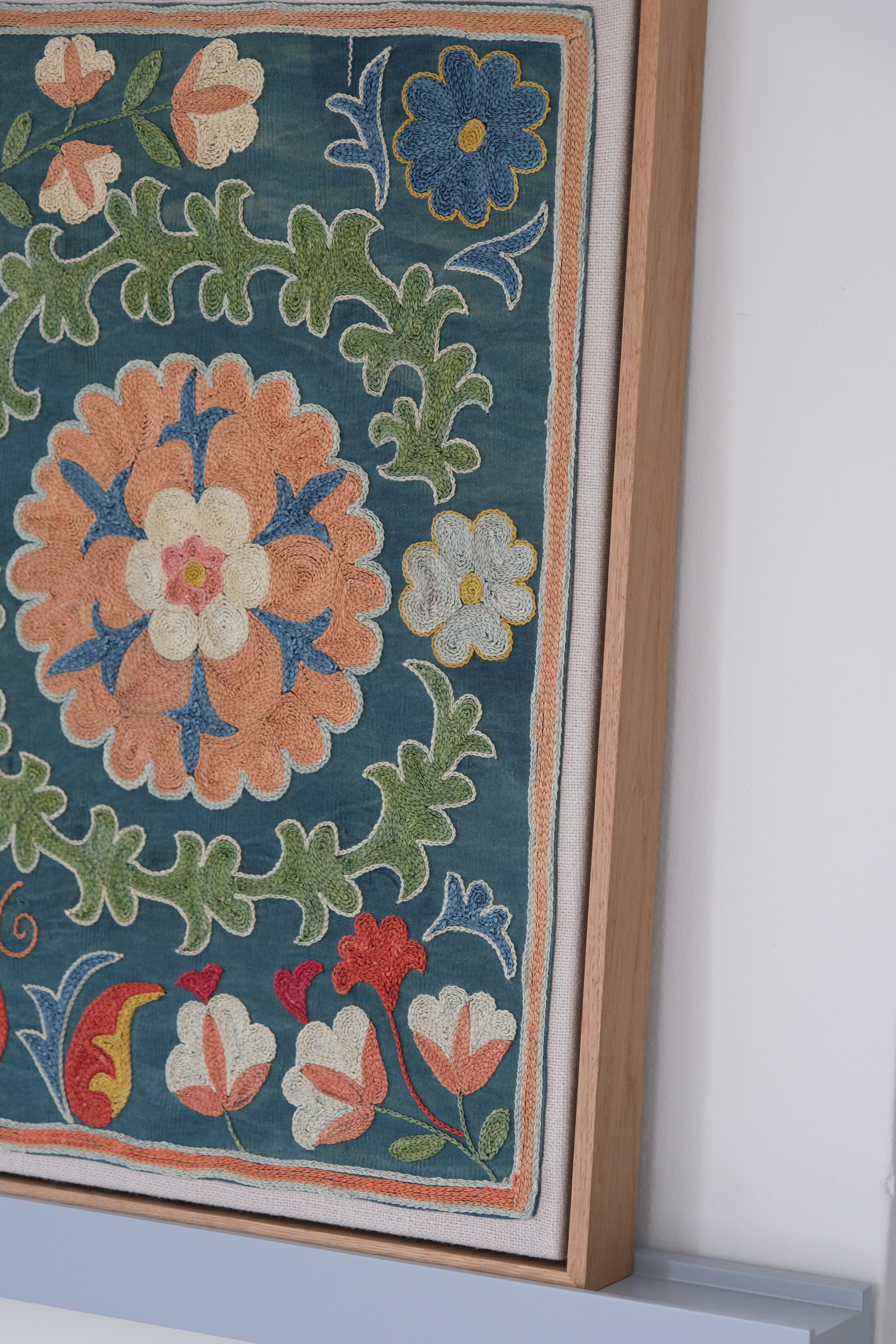 Framed suzani, embroidered textile art, wooden frame, green with orange and blue floral motifs, side view
