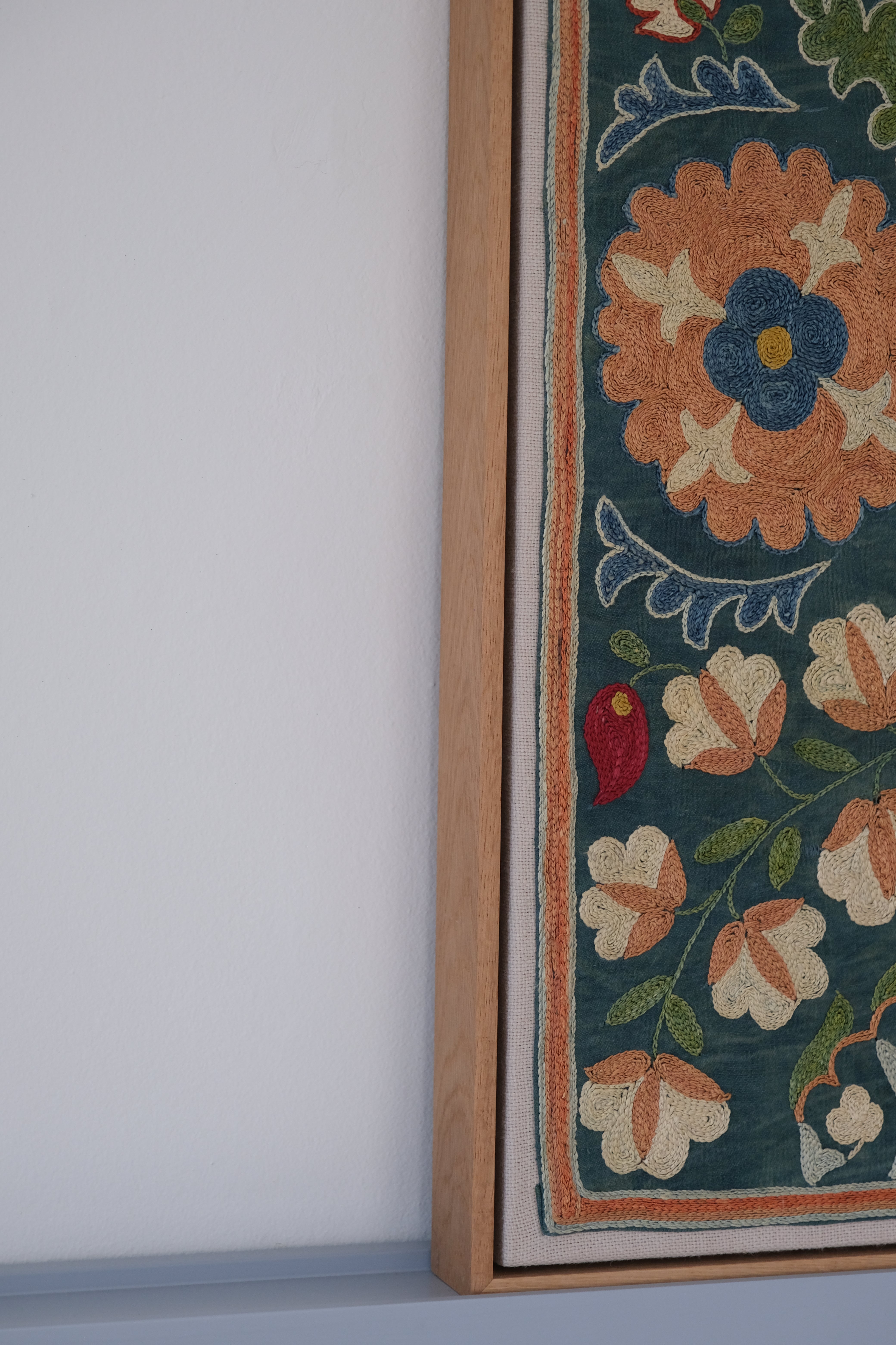 Framed suzani, embroidered textile art, wooden frame, green with orange and blue floral motifs, side view