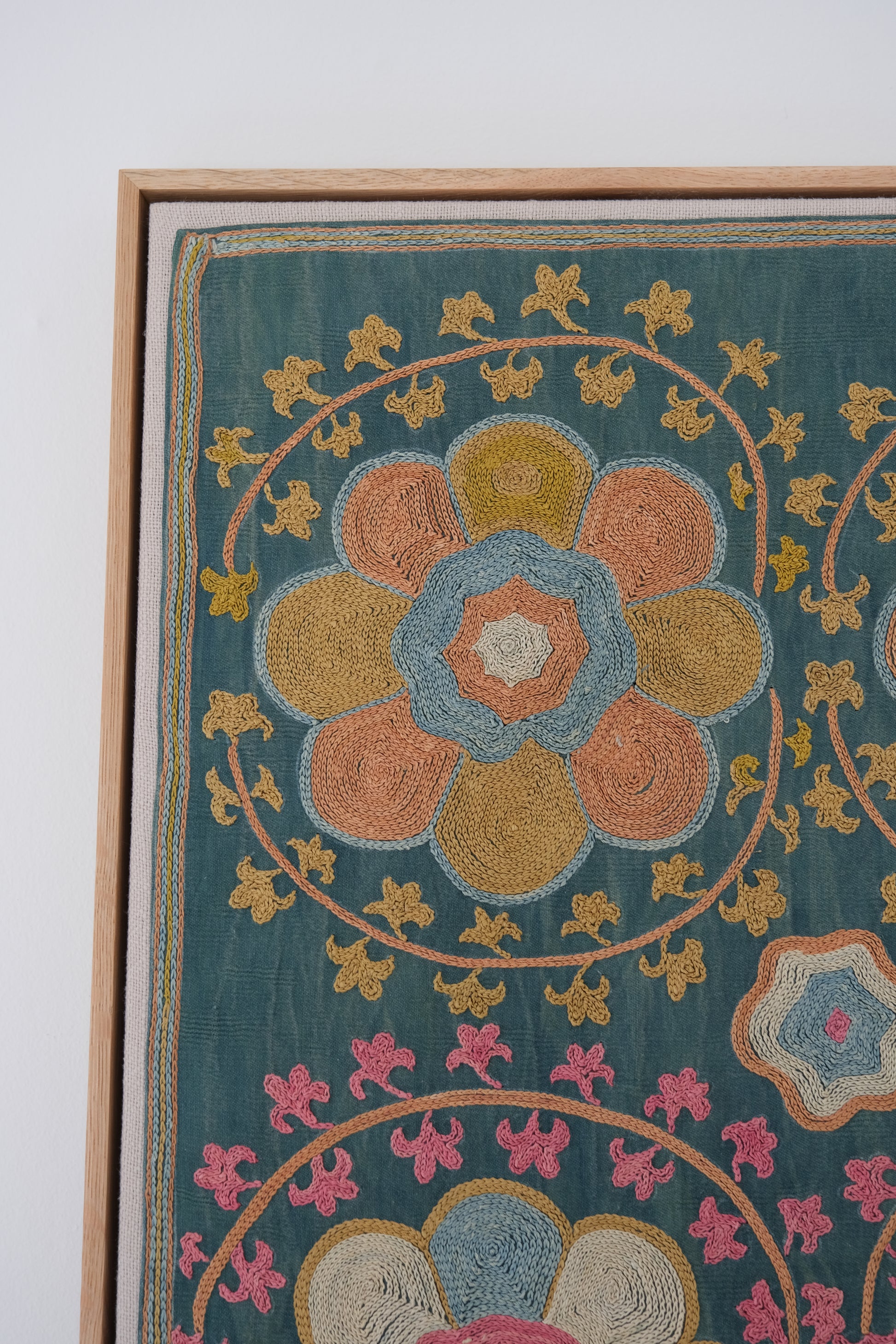 Framed suzani, embroidered textile art, wooden frame, green with orange and pink floral motifs, close-up