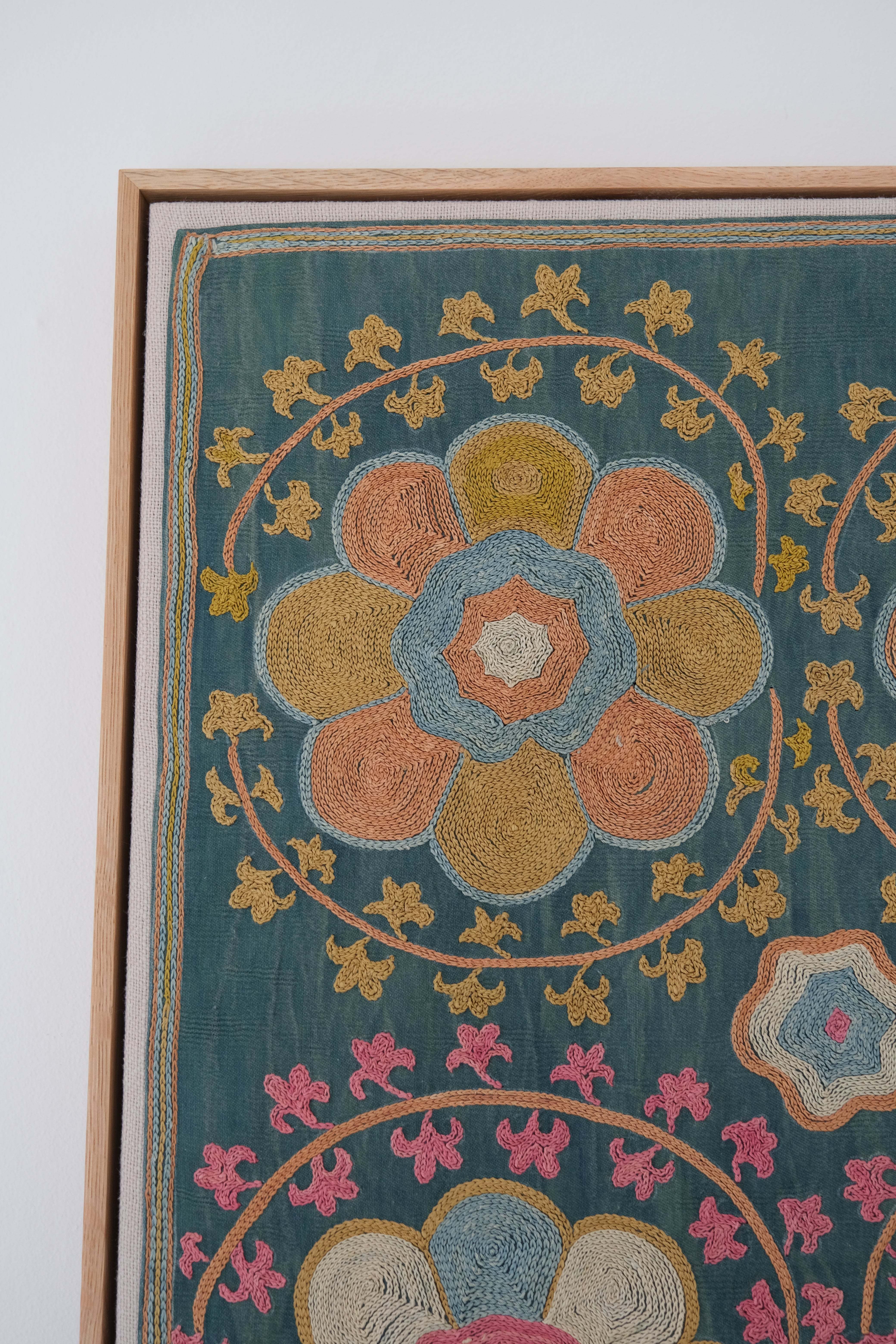 Framed suzani, embroidered textile art, wooden frame, green with orange and pink floral motifs, close-up