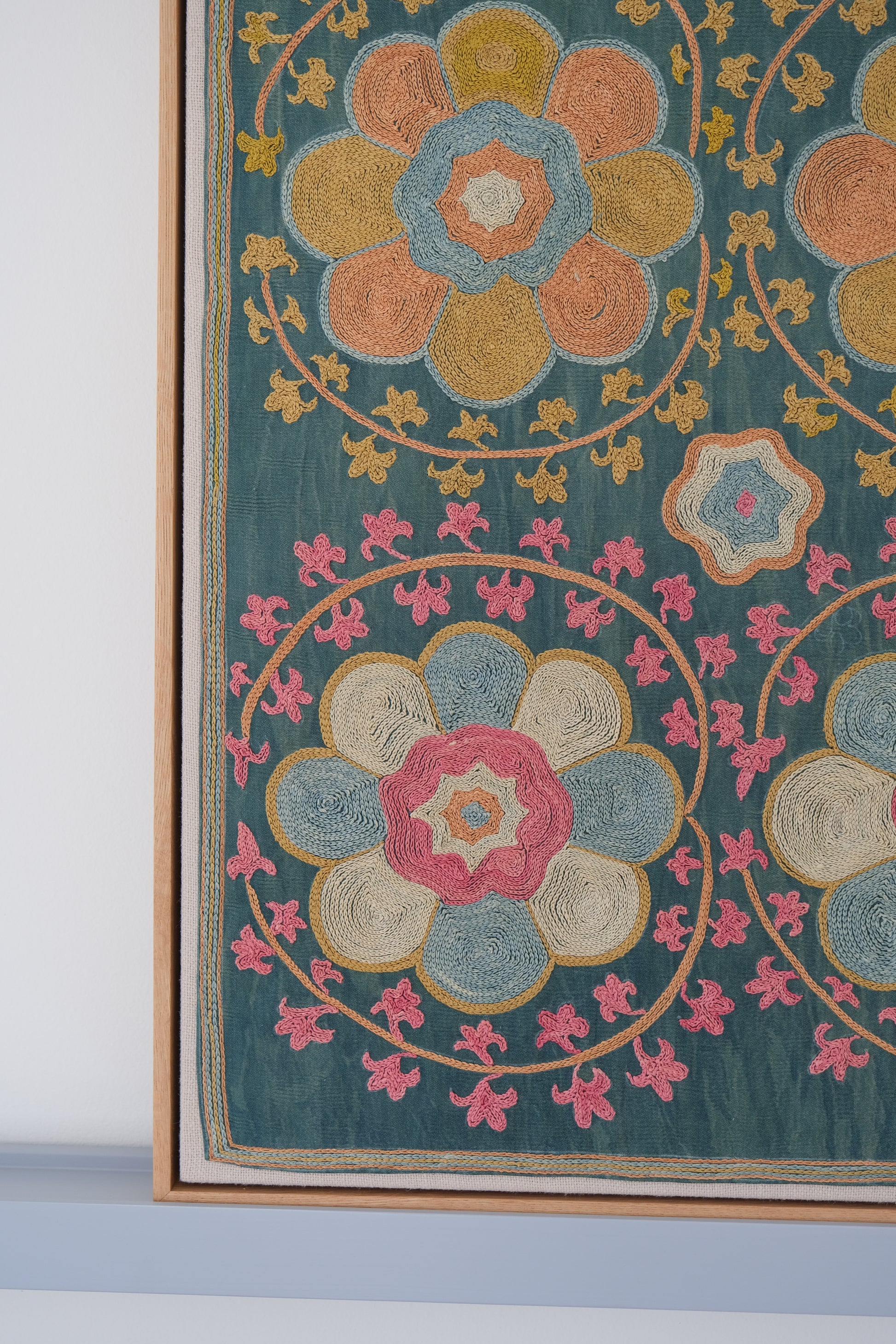 Framed suzani, embroidered textile art, wooden frame, green with orange and pink floral motifs, close-up