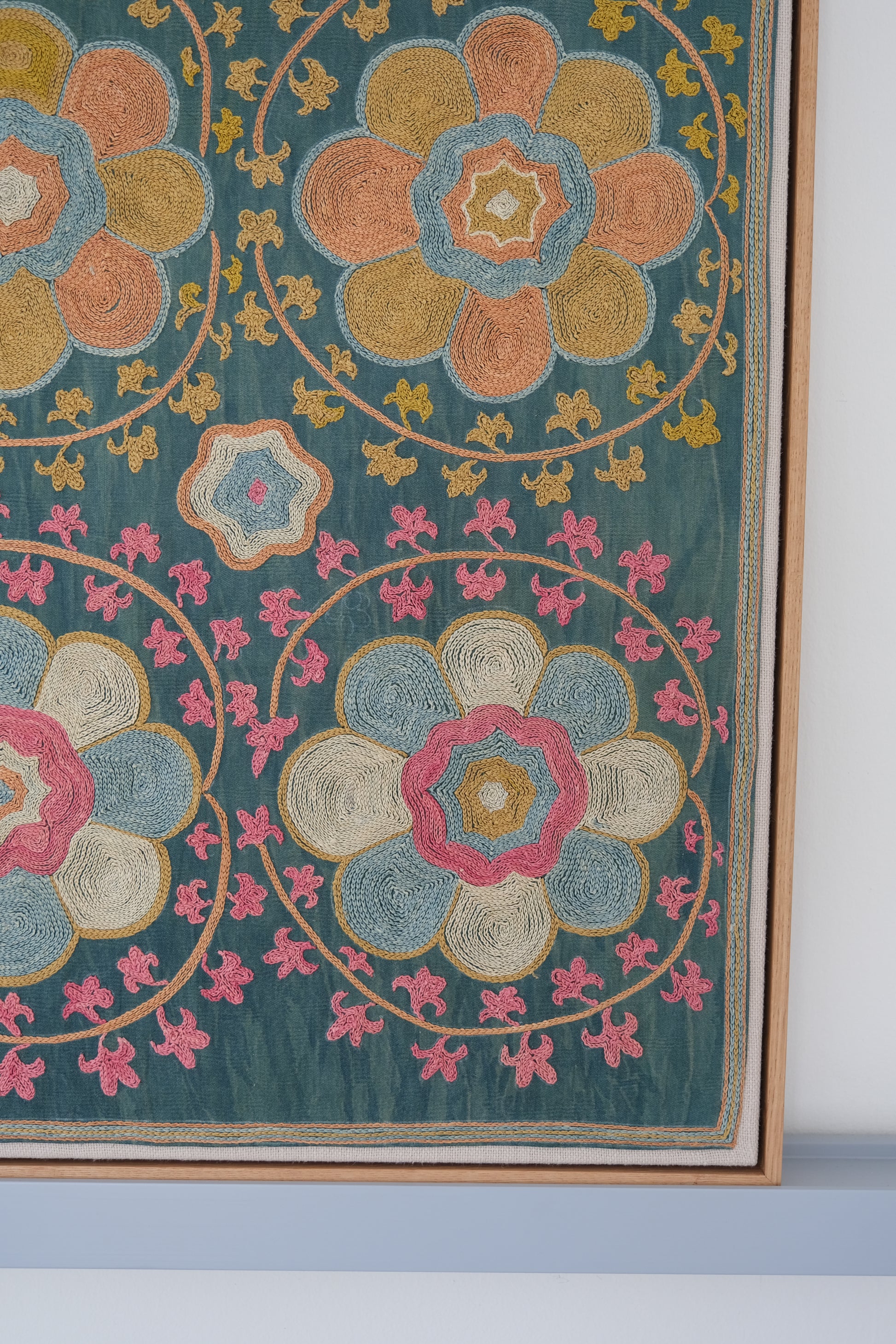 Framed suzani, embroidered textile art, wooden frame, green with orange and pink floral motifs, close-up