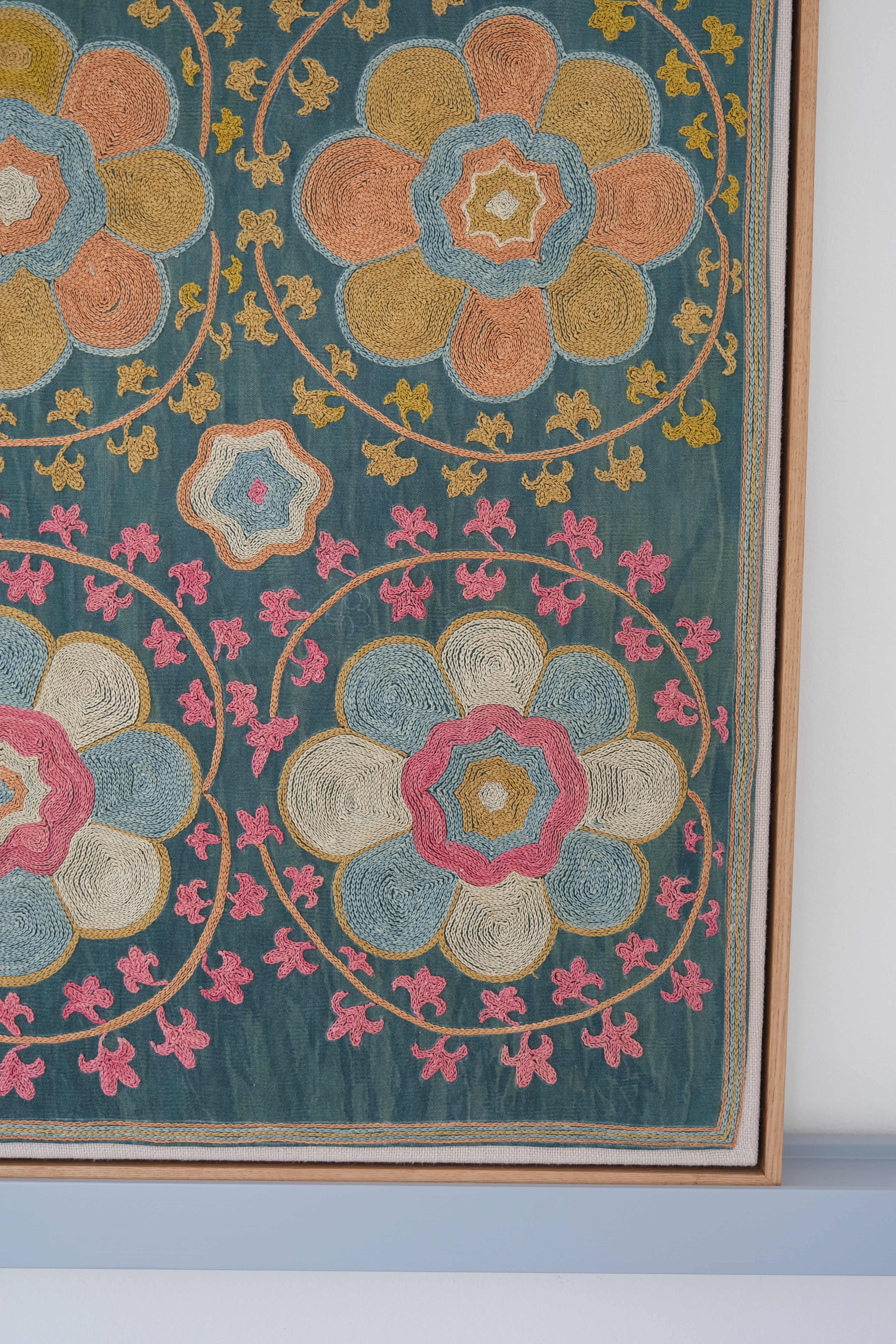 Framed suzani, embroidered textile art, wooden frame, green with orange and pink floral motifs, close-up