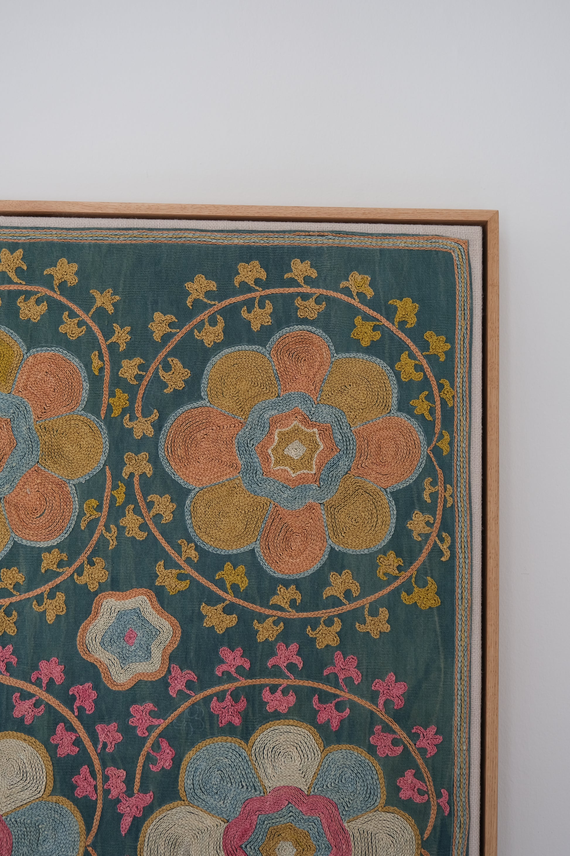 Framed suzani, embroidered textile art, wooden frame, green with orange and pink floral motifs, close-up