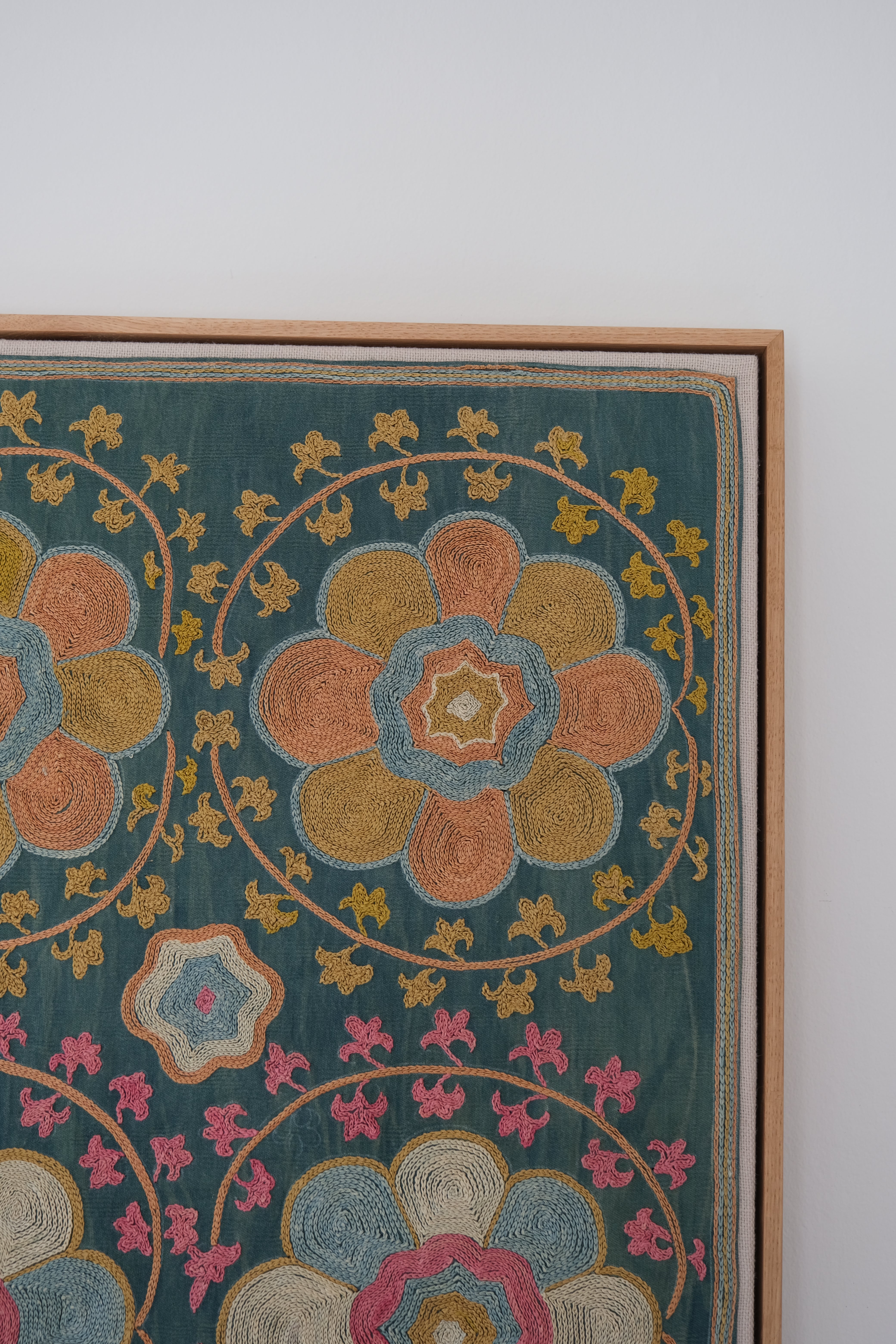 Framed suzani, embroidered textile art, wooden frame, green with orange and pink floral motifs, close-up