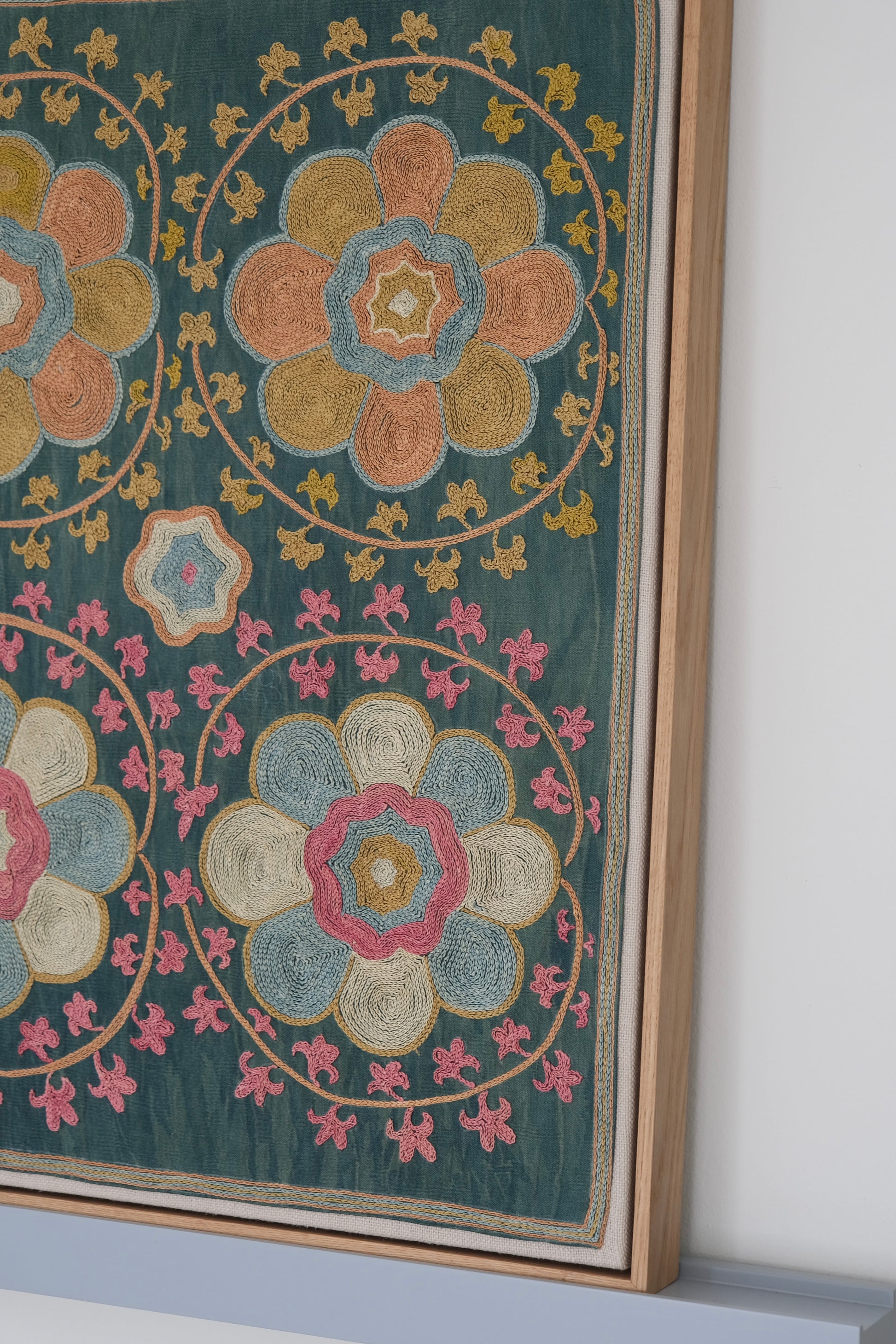 Framed suzani, embroidered textile art, wooden frame, green with orange and pink floral motifs, side view