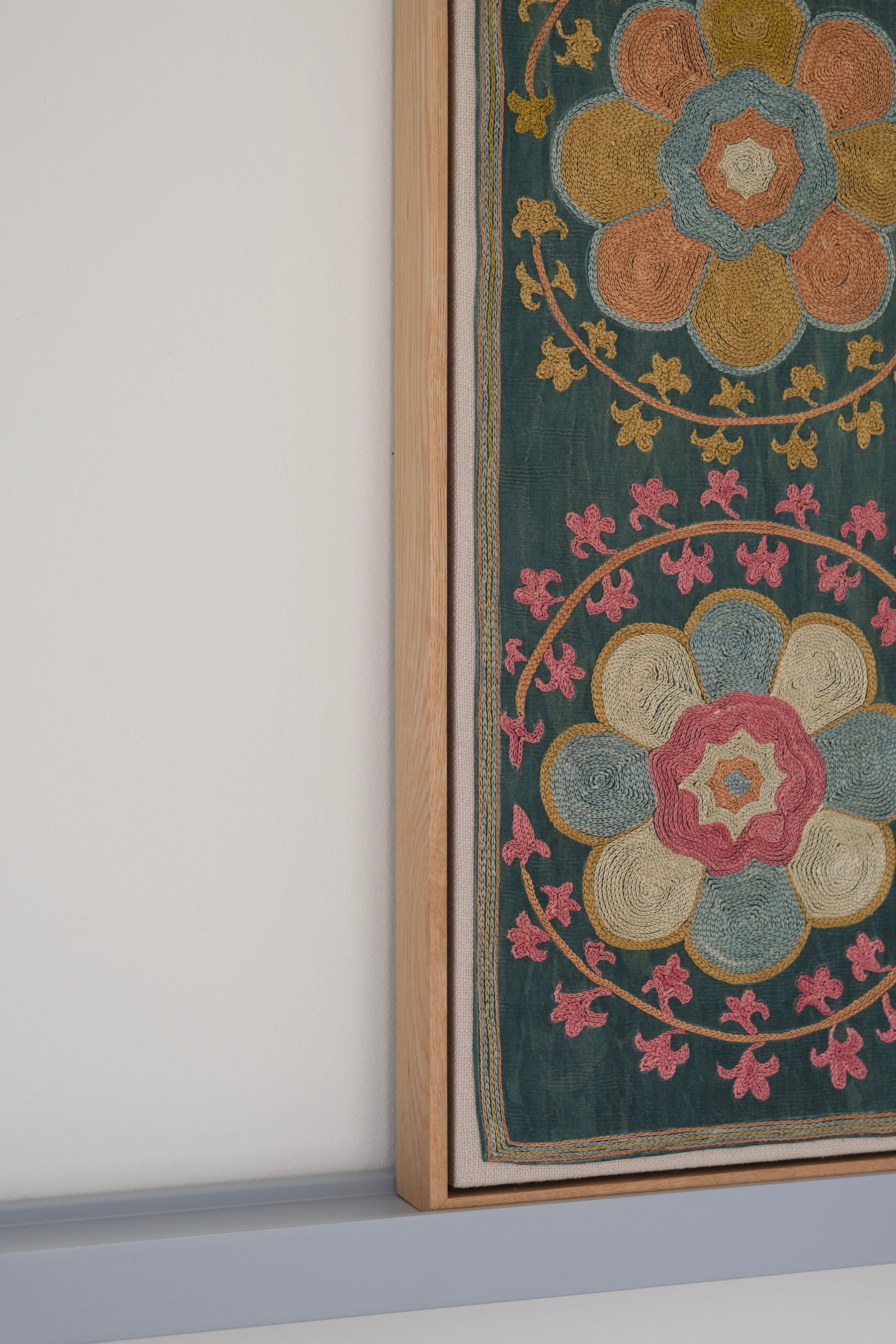 Framed suzani, embroidered textile art, wooden frame, green with orange and pink floral motifs, side view
