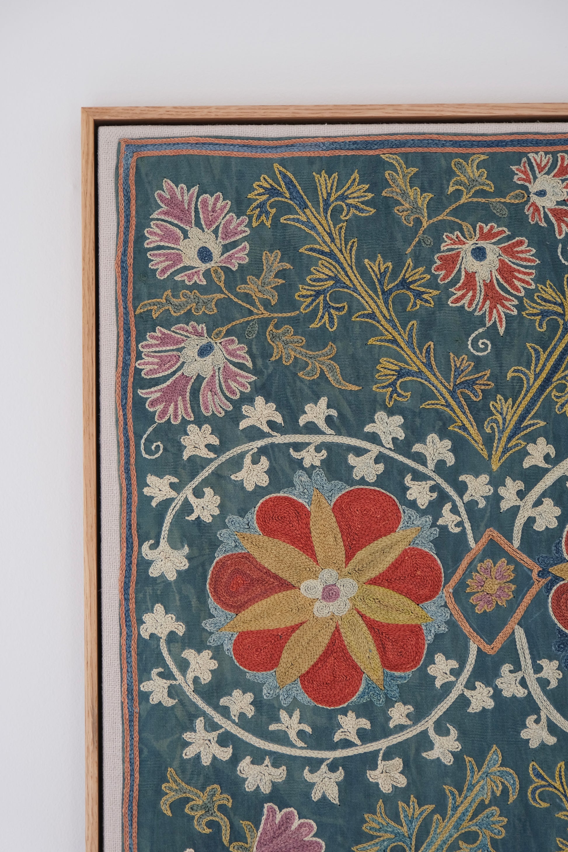 Framed suzani, embroidered textile art, wooden frame, green with floral motifs, close-up
