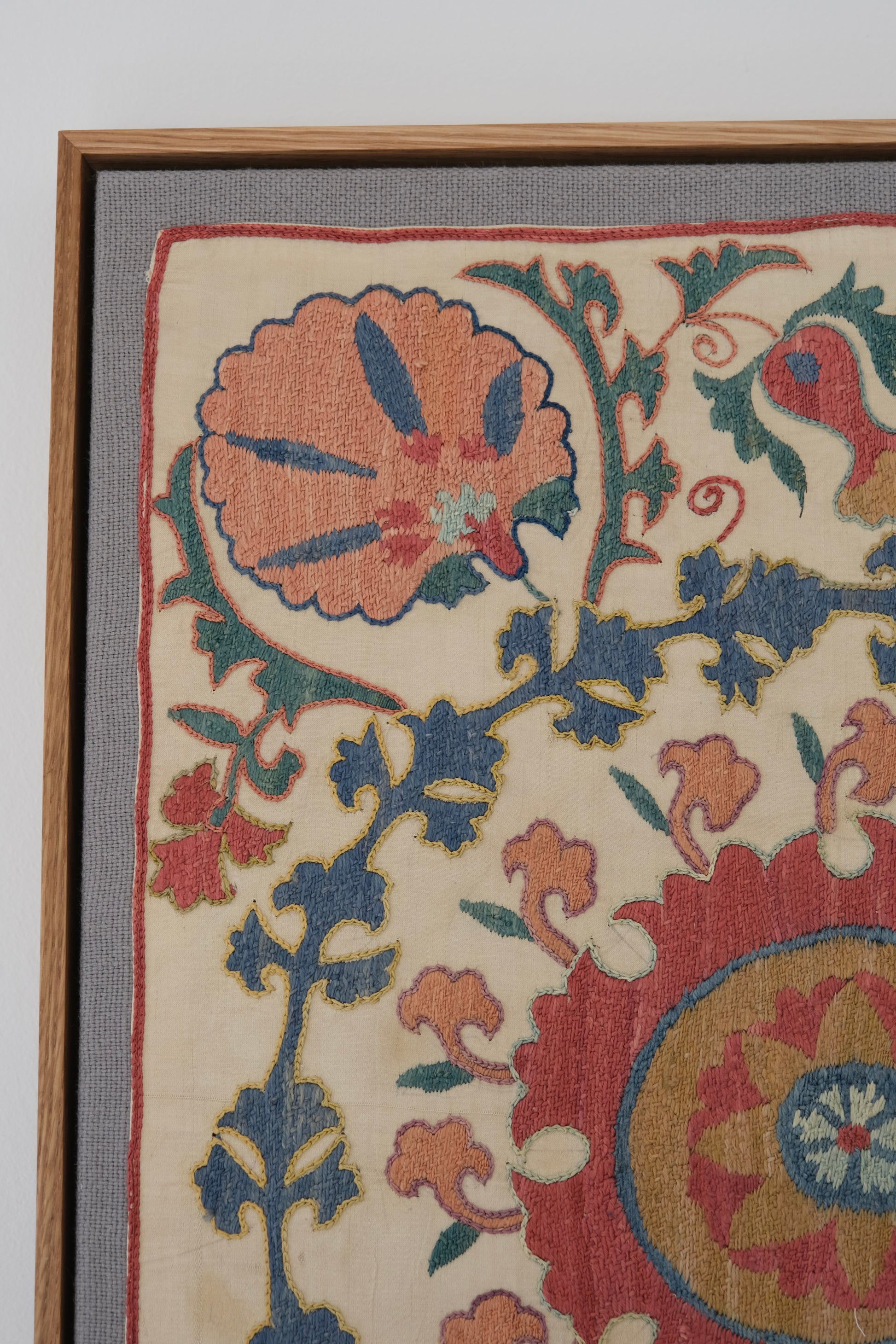 Framed suzani, embroidered textile art, wooden frame, white with pink and blue design, close-up