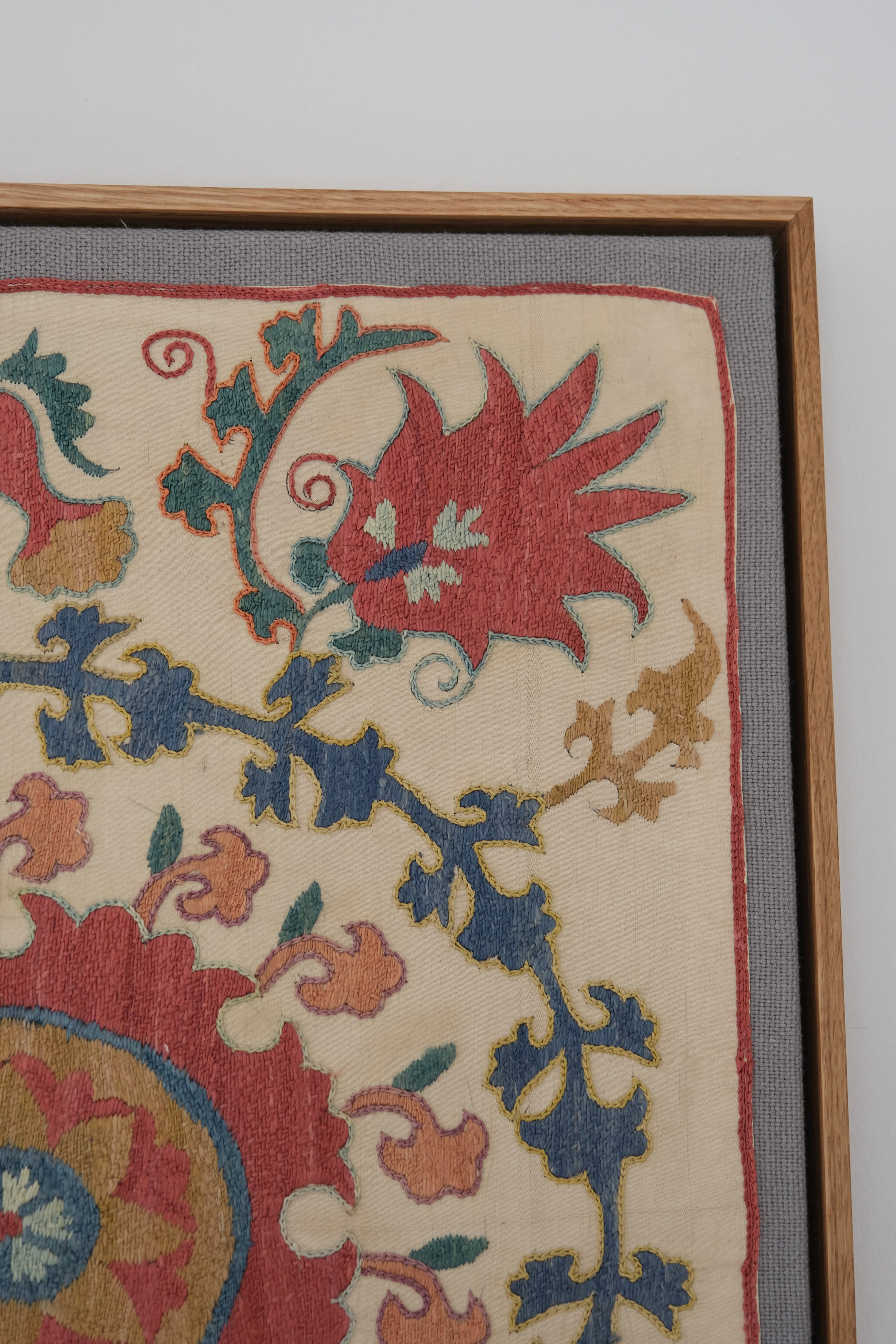 Framed suzani, embroidered textile art, wooden frame, white with pink and blue design, close-up