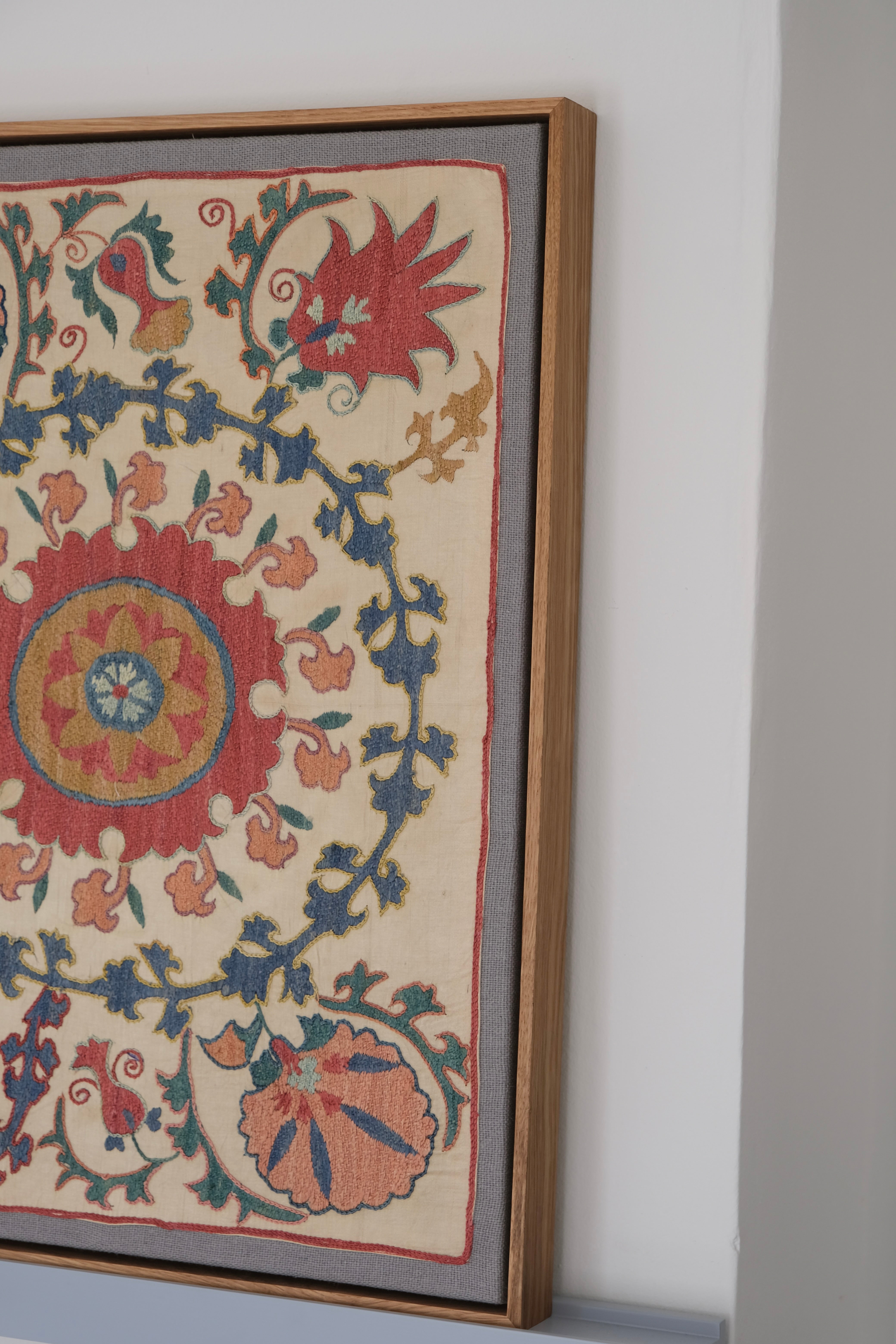 Framed suzani, embroidered textile art, wooden frame, white with pink and blue design, side view