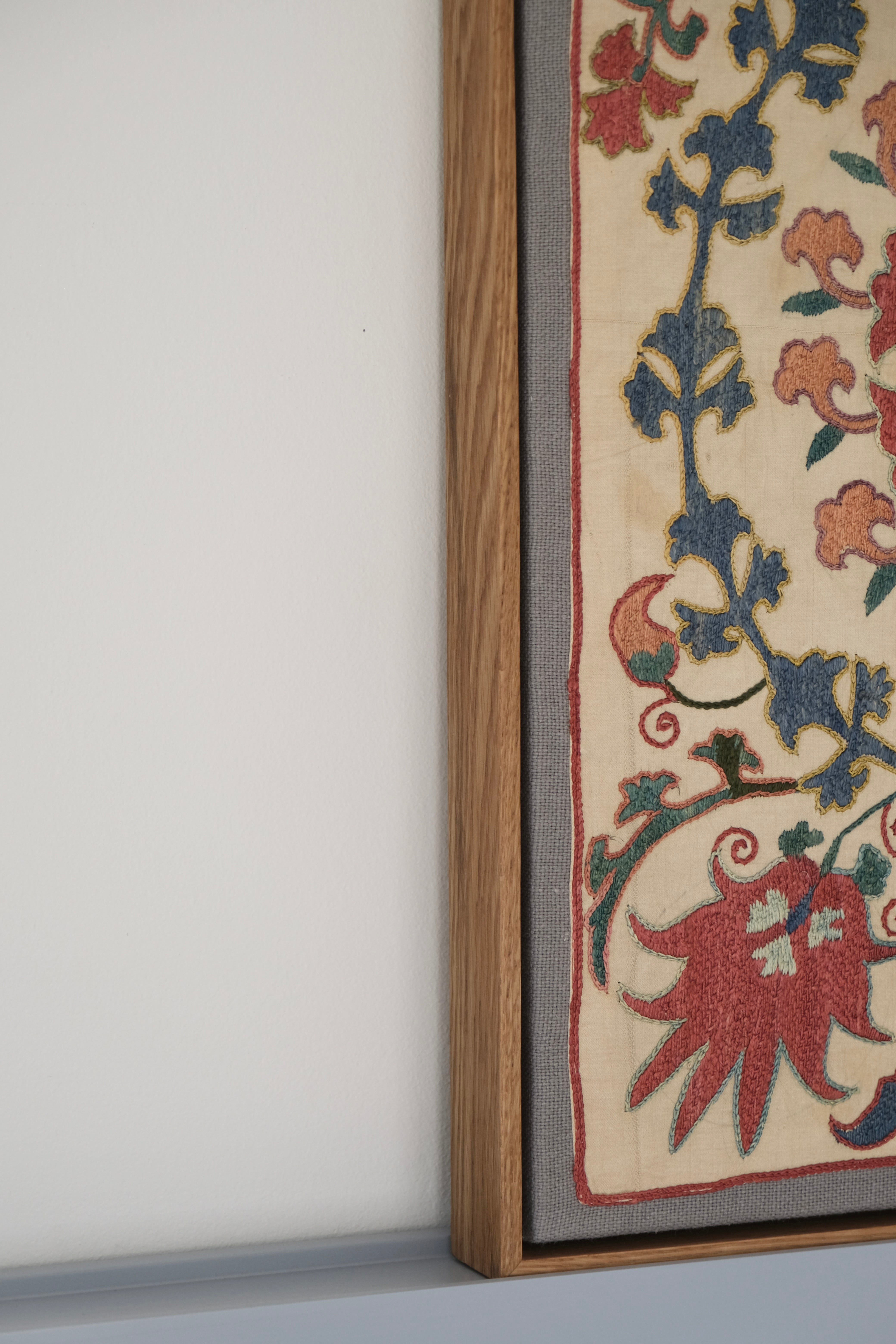 Framed suzani, embroidered textile art, wooden frame, white with pink and blue design, side view