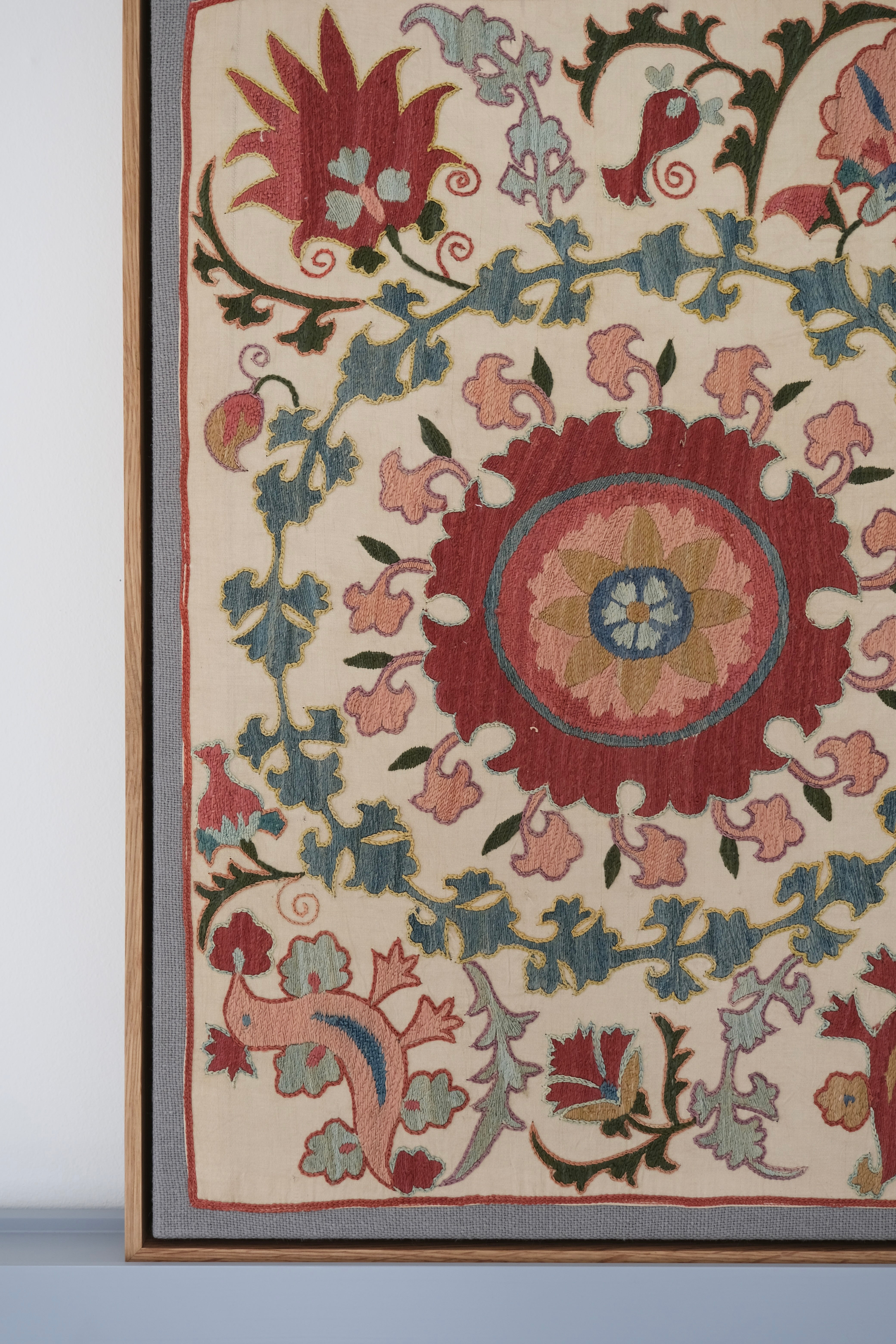 Framed suzani, embroidered textile art, wooden frame, white with pink and blue bird design, close-up