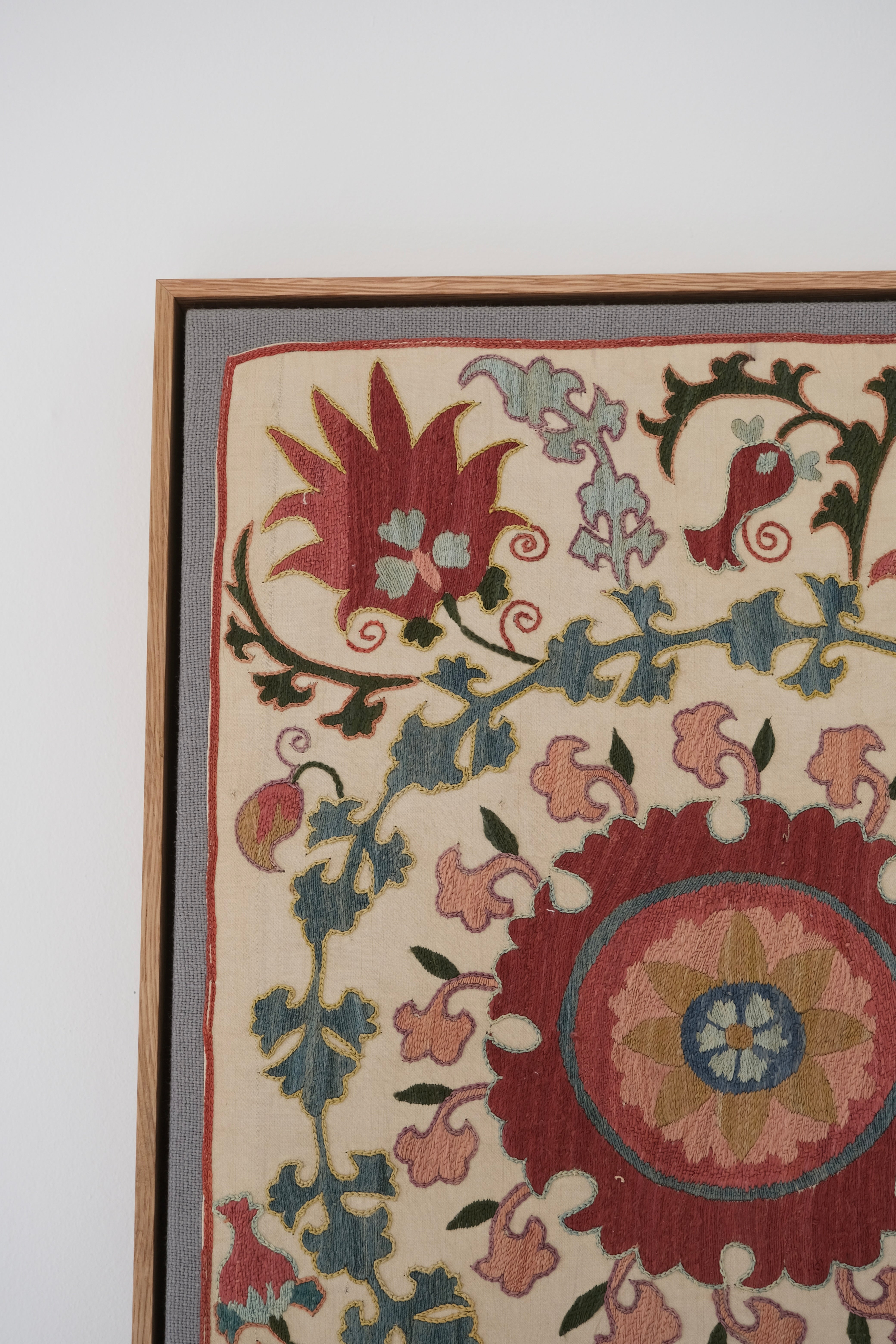 Framed suzani, embroidered textile art, wooden frame, white with pink and blue bird design, close-up