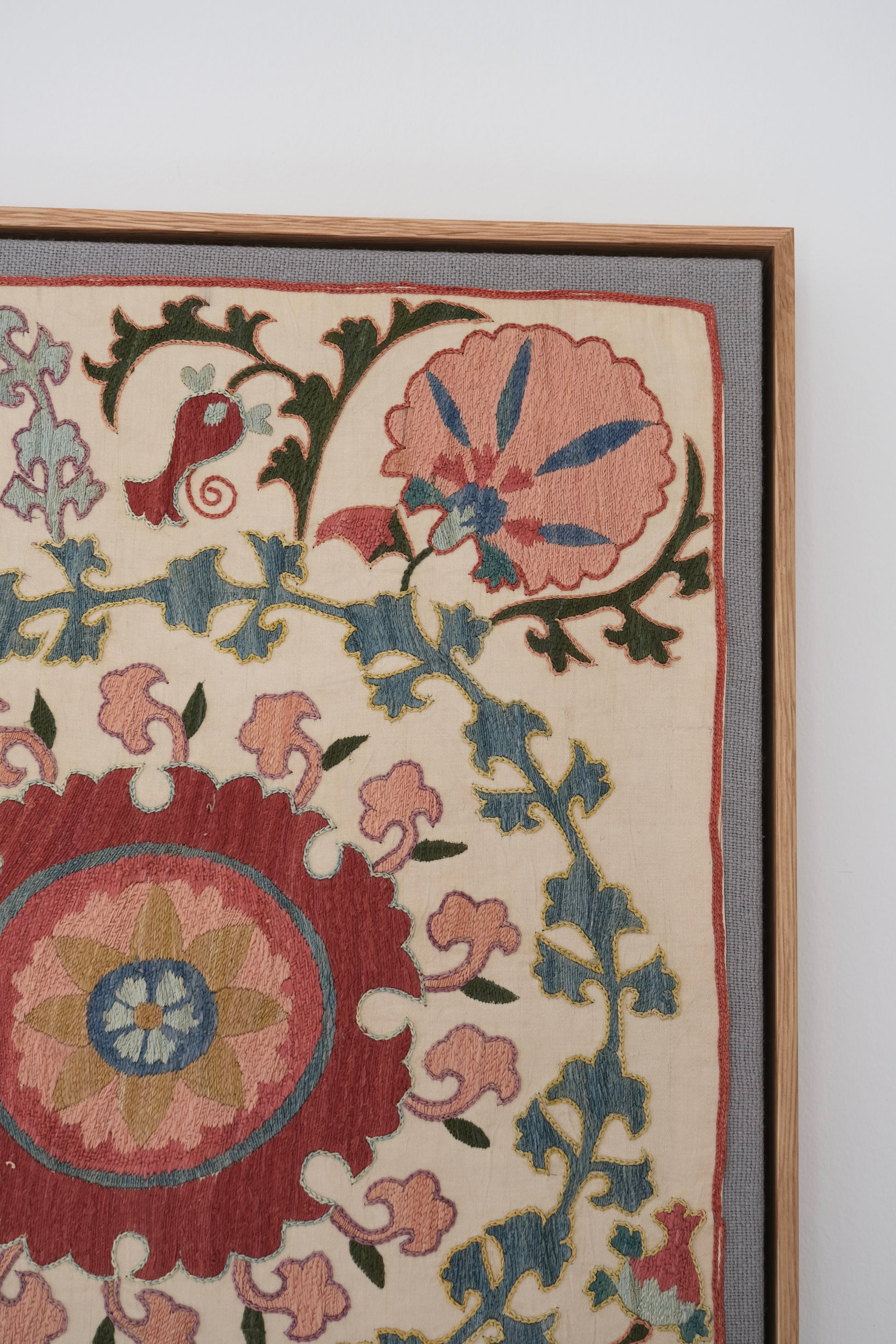 Framed suzani, embroidered textile art, wooden frame, white with pink and blue bird design, close-up