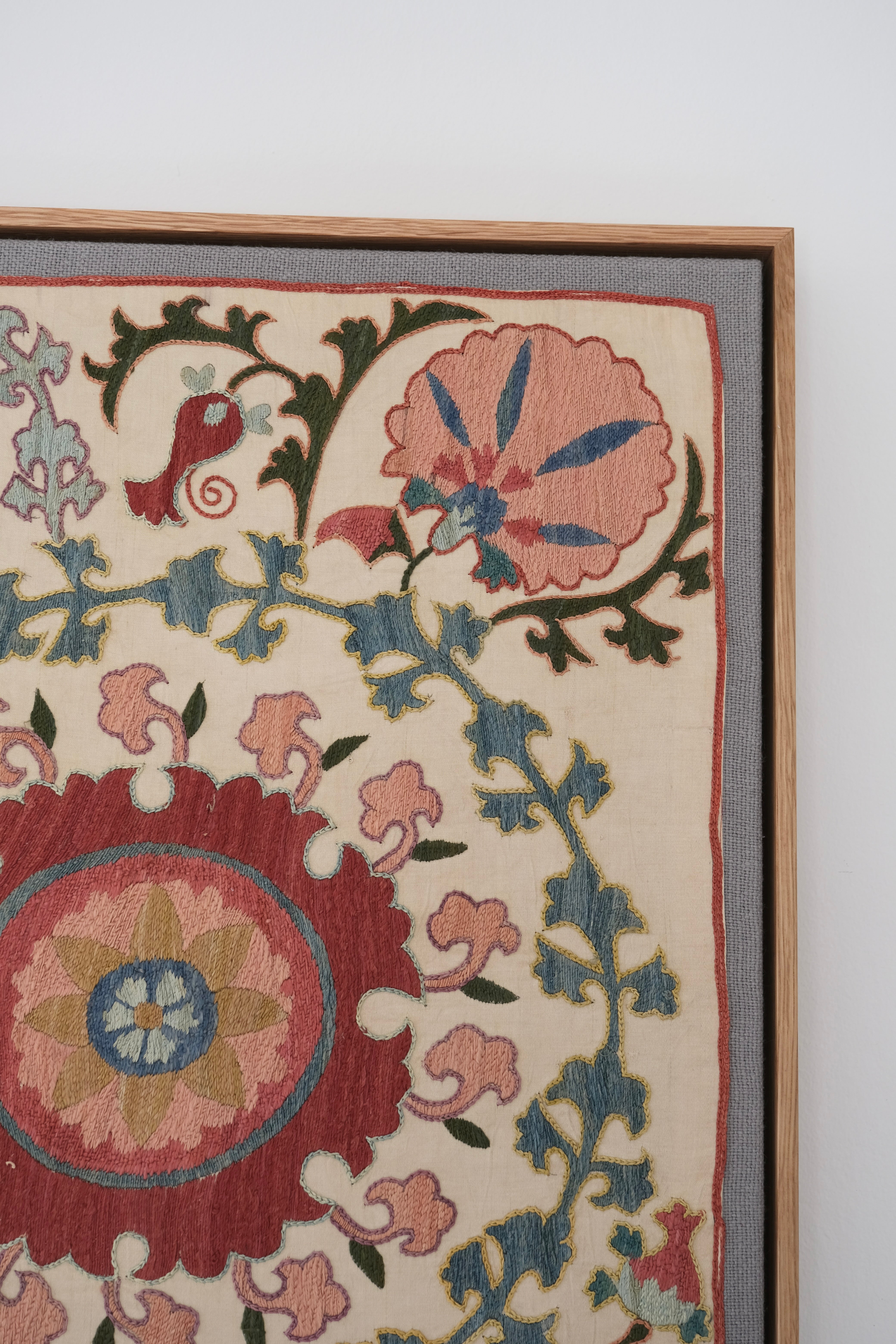 Framed suzani, embroidered textile art, wooden frame, white with pink and blue bird design, close-up