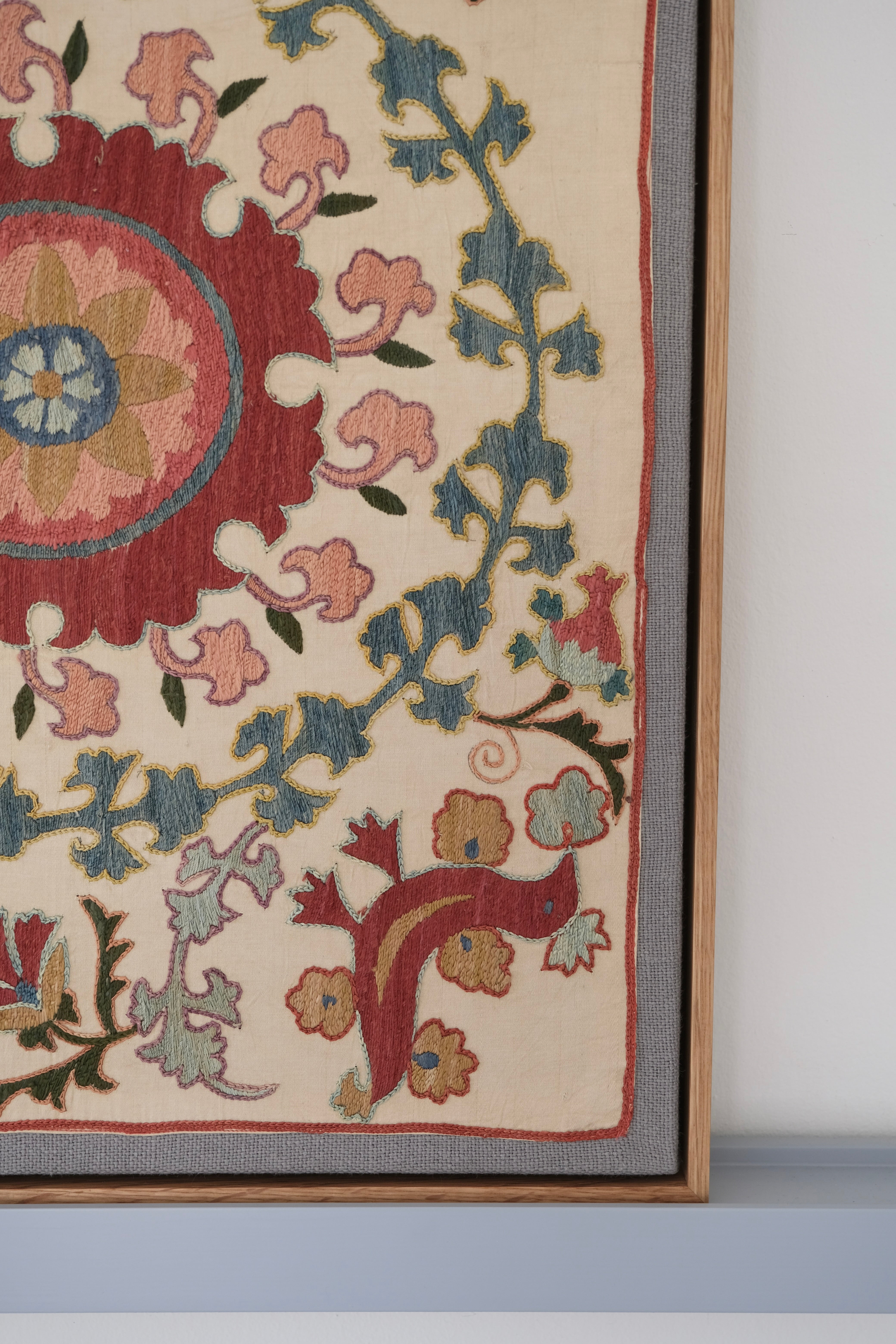 Framed suzani, embroidered textile art, wooden frame, white with pink and blue bird design, close-up