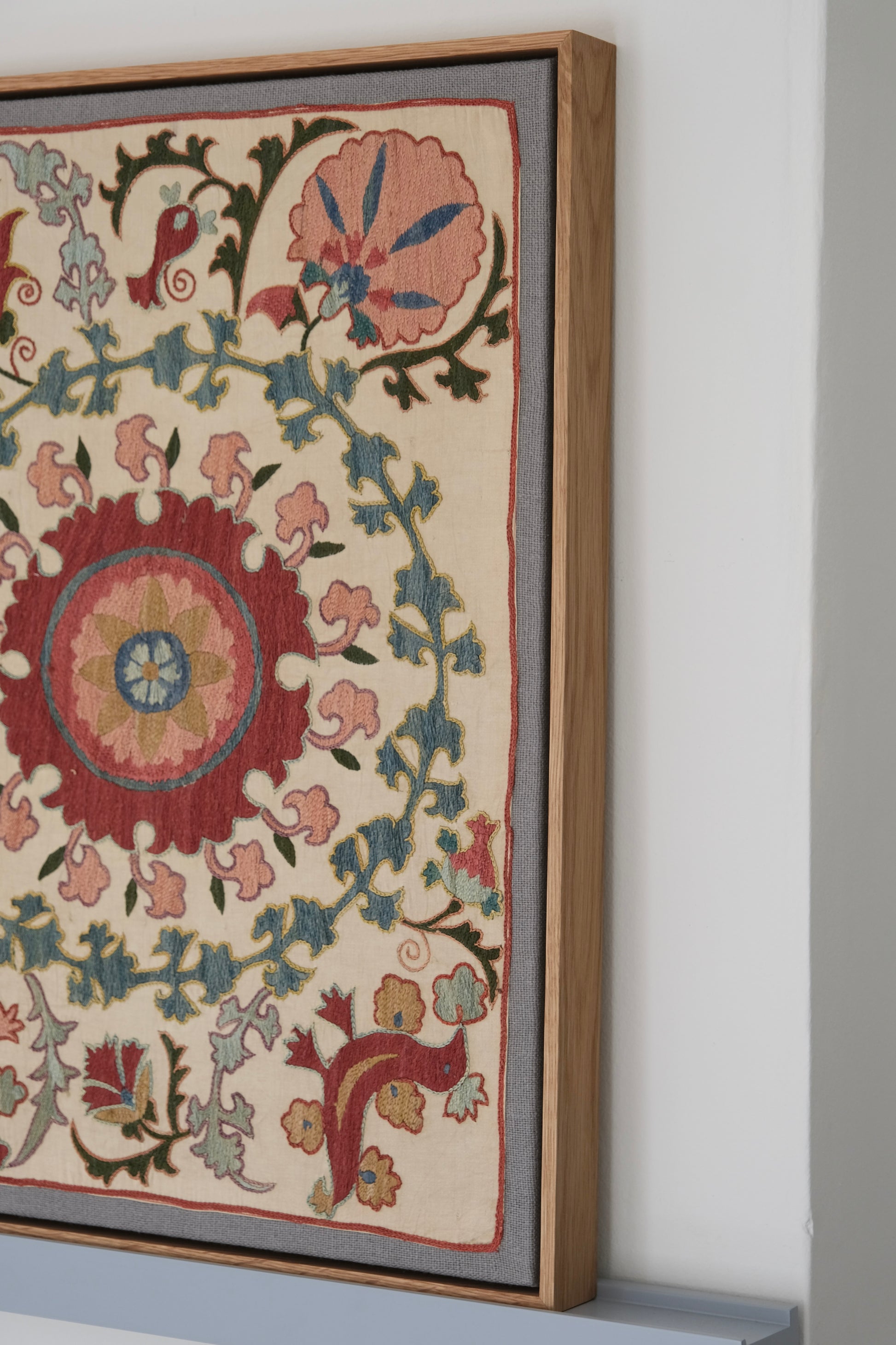 Framed suzani, embroidered textile art, wooden frame, white with pink and blue bird design, side view