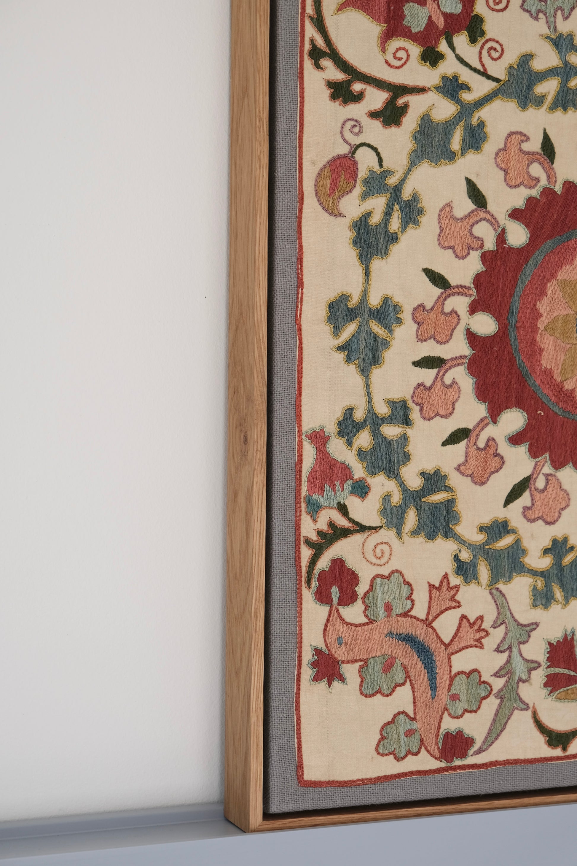 Framed suzani, embroidered textile art, wooden frame, white with pink and blue bird design, side view