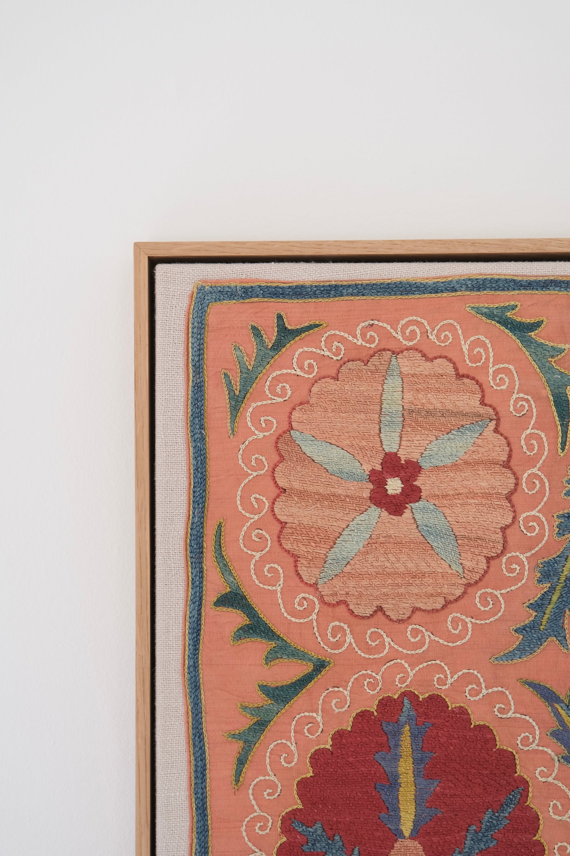 Framed suzani, embroidered textile art, wooden frame, light orange with red and blue floral motifs, close-up