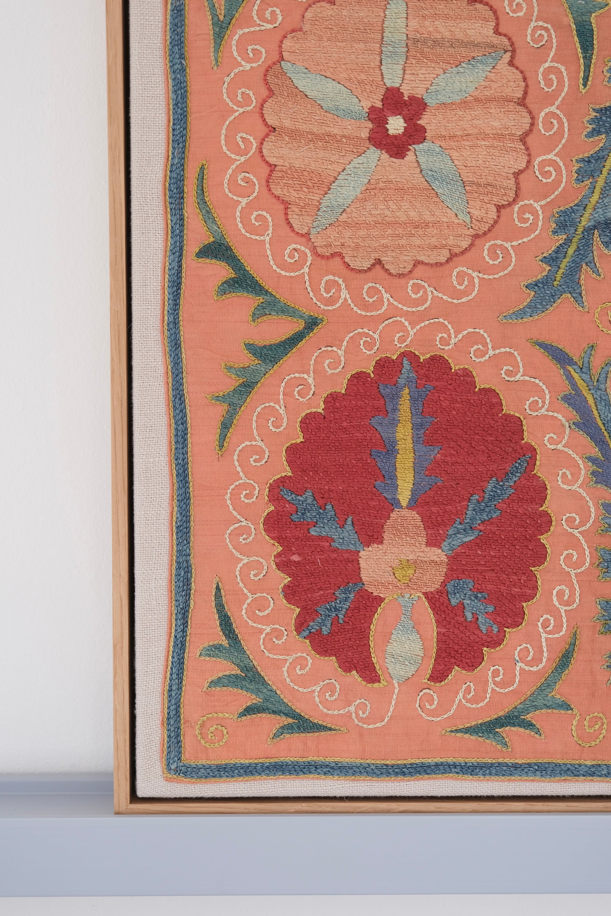 Framed suzani, embroidered textile art, wooden frame, light orange with red and blue floral motifs, close-up