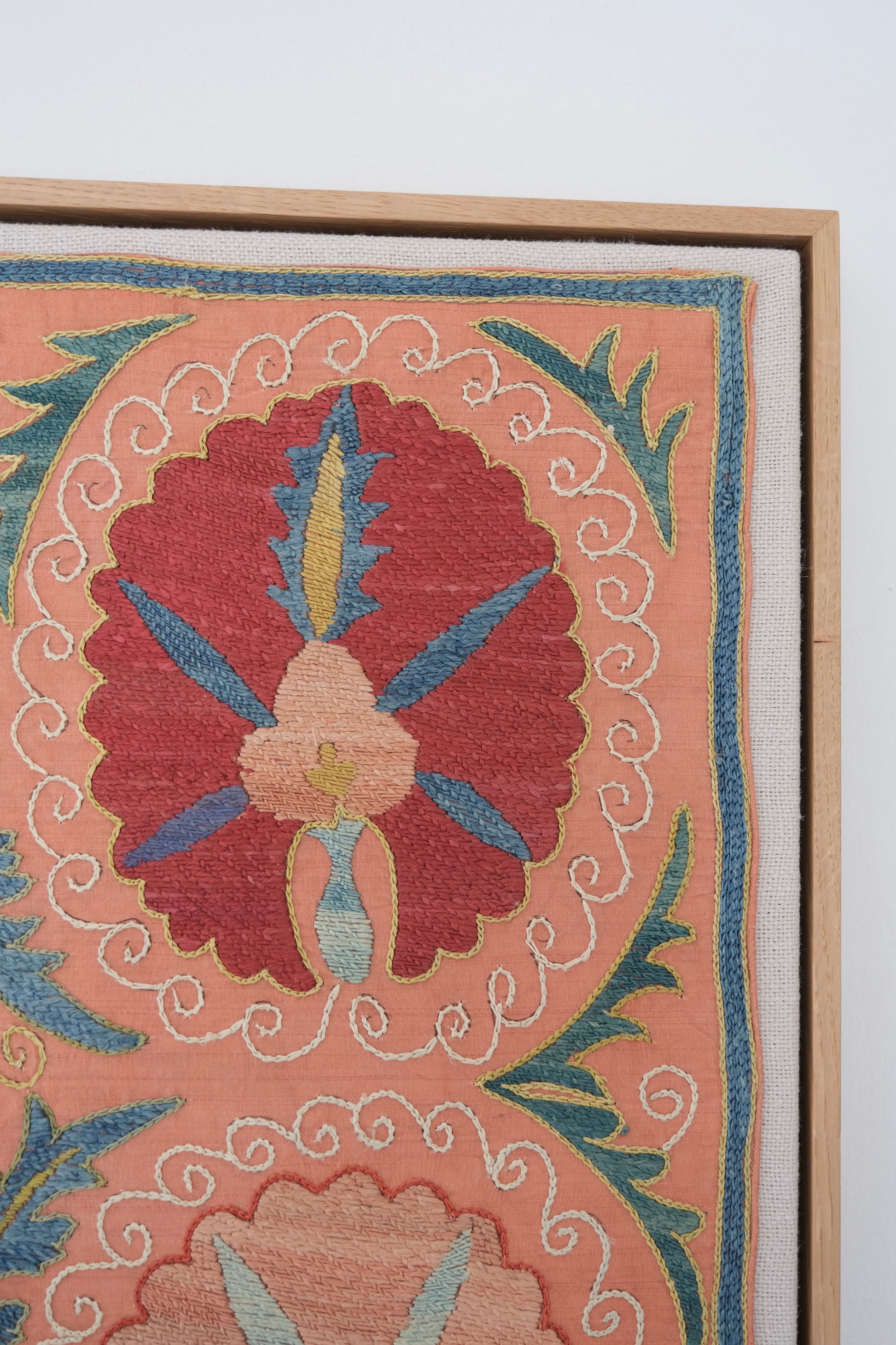 Framed suzani, embroidered textile art, wooden frame, light orange with red and blue floral motifs, close-up