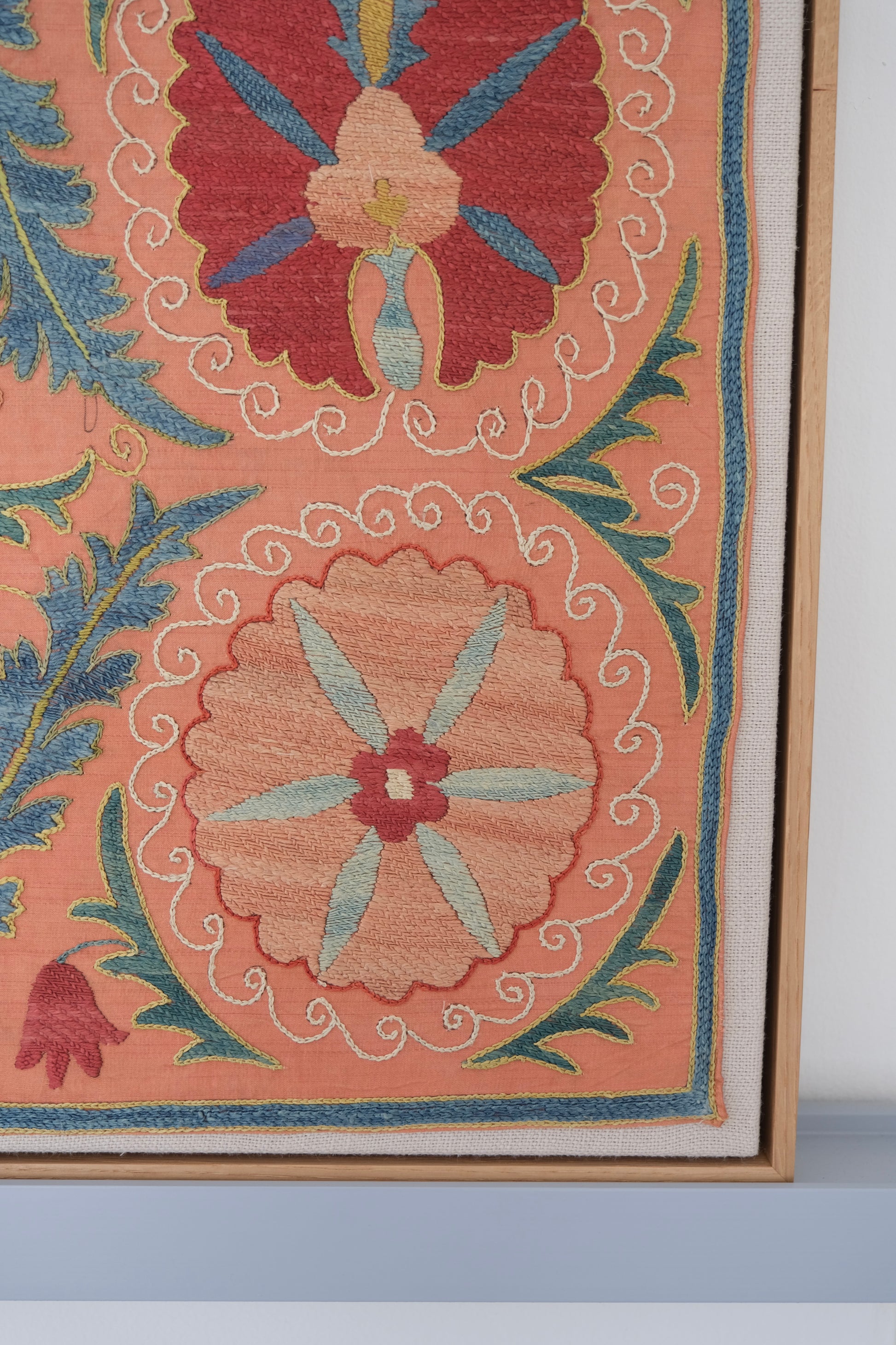 Framed suzani, embroidered textile art, wooden frame, light orange with red and blue floral motifs, close-up